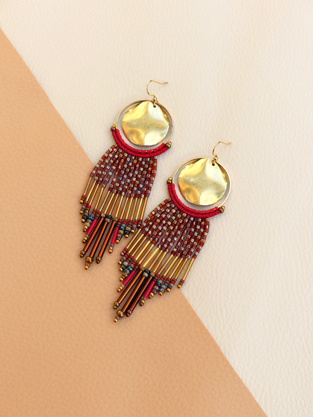 Peut inclure: Une paire de longues boucles d'oreilles en perles avec des accents dorés. Les boucles d'oreilles présentent un schéma de couleurs rouge et or et un disque rond en or martelé en haut.