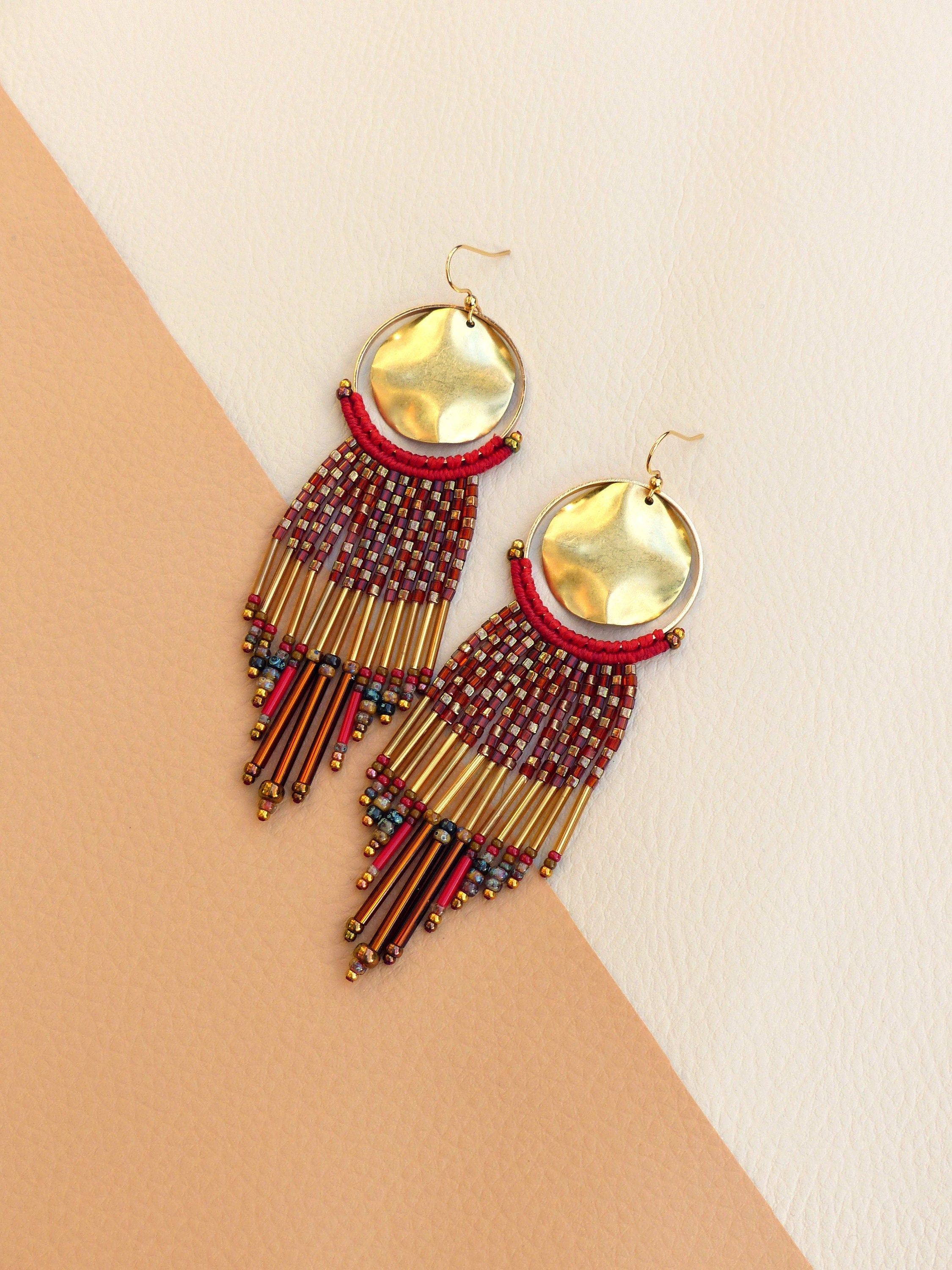 Peut inclure: Une paire de longues boucles d'oreilles en perles avec des accents dorés. Les boucles d'oreilles présentent un schéma de couleurs rouge et or et un disque rond en or martelé en haut.