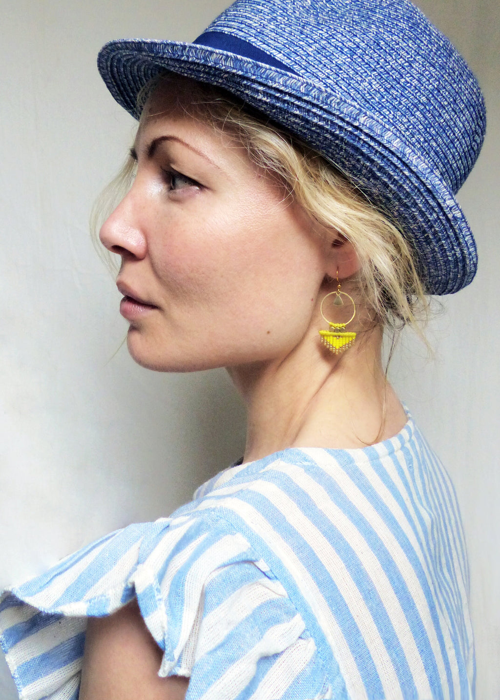 Peut inclure: Une femme portant une chemise rayée bleu et blanc avec un chapeau de paille bleu. Elle porte des boucles d'oreilles créoles jaunes et dorées.