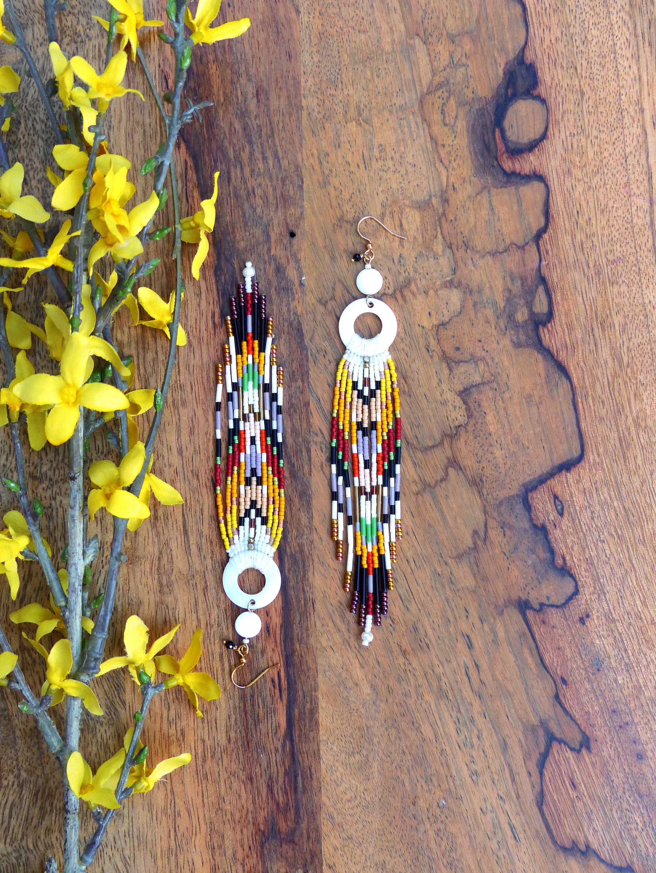 Peut inclure: Une paire de longues boucles d'oreilles en perles colorées avec des accents circulaires blancs. Les boucles d'oreilles sont faites de petites perles colorées et ont un design en forme de frange.