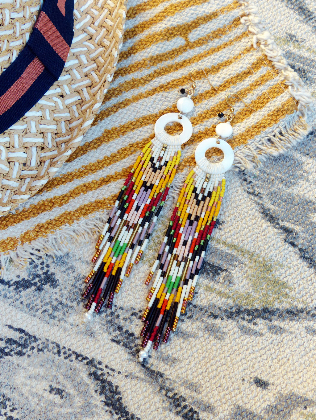 Peut inclure: Une paire de longues boucles d'oreilles en perles colorées avec des pendentifs circulaires blancs. Les boucles d'oreilles présentent une variété de couleurs, notamment le rouge, le jaune, le vert, le bleu et le noir.
