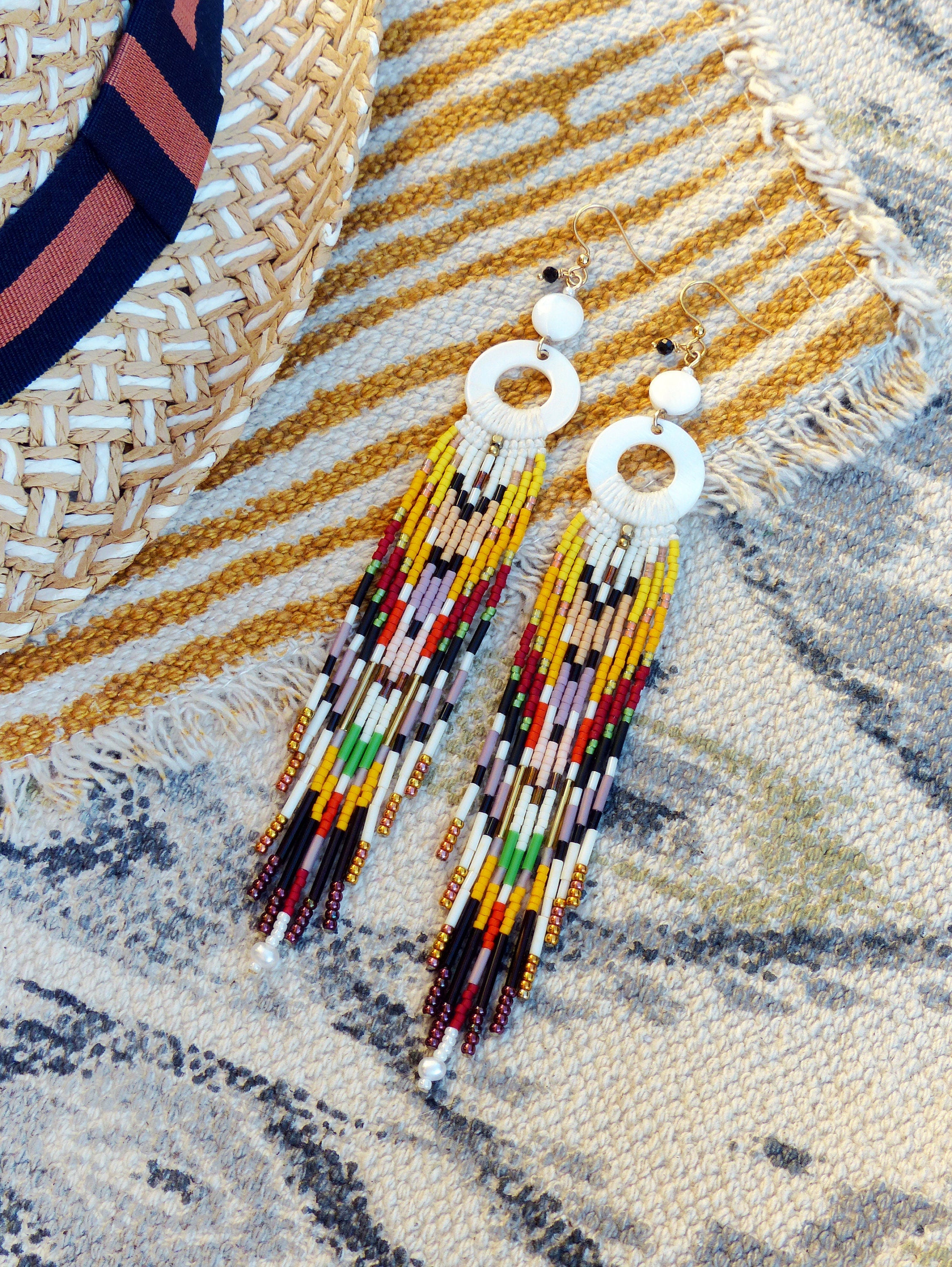 Peut inclure: Une paire de longues boucles d'oreilles en perles colorées avec des pendentifs circulaires blancs. Les boucles d'oreilles présentent une variété de couleurs, notamment le rouge, le jaune, le vert, le bleu et le noir.