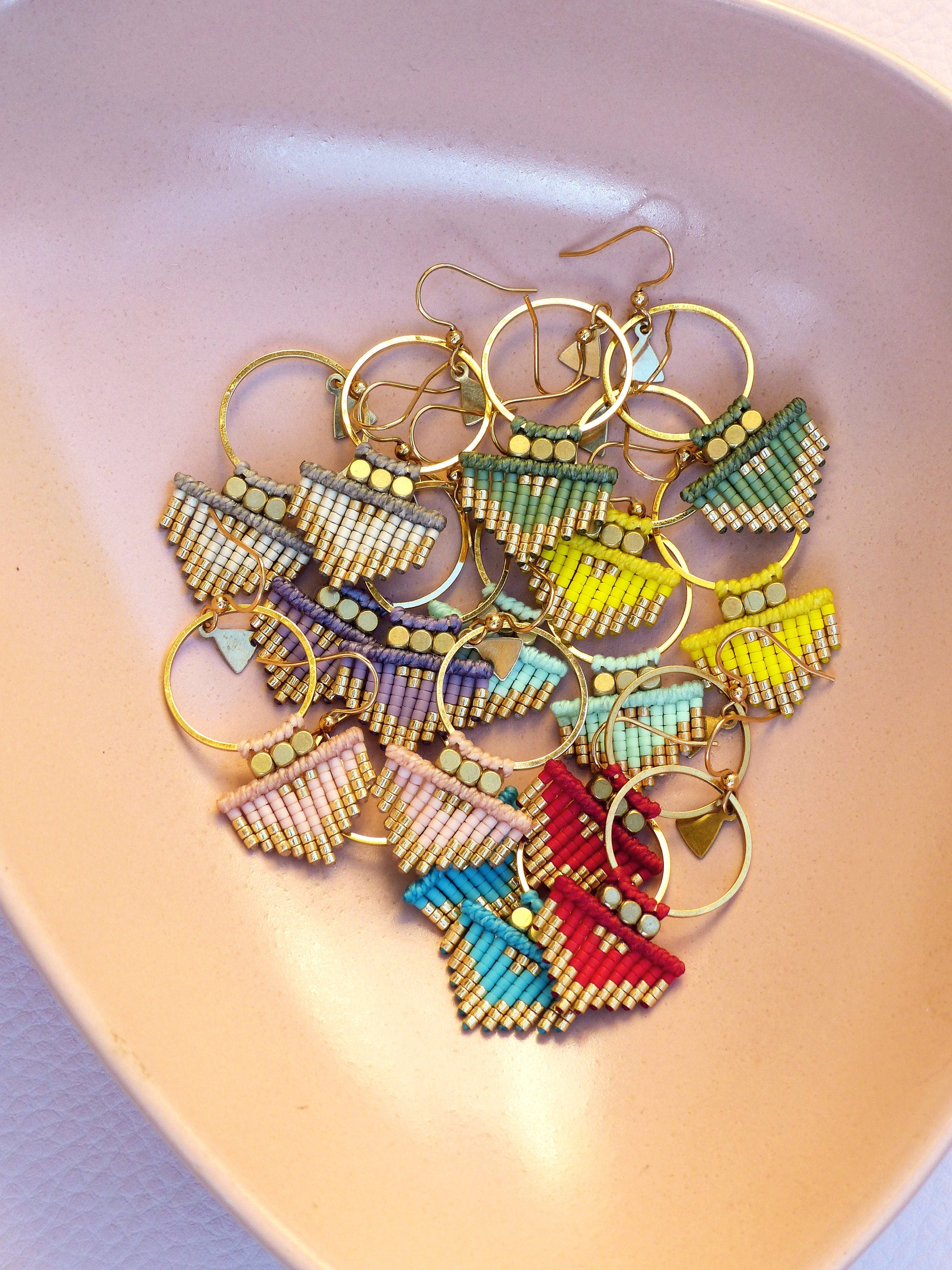 Peut inclure: Une collection de boucles d'oreilles en perles colorées avec des cercles dorés. Les boucles d'oreilles présentent une variété de couleurs, notamment le rose, le bleu, le vert, le jaune et le violet.