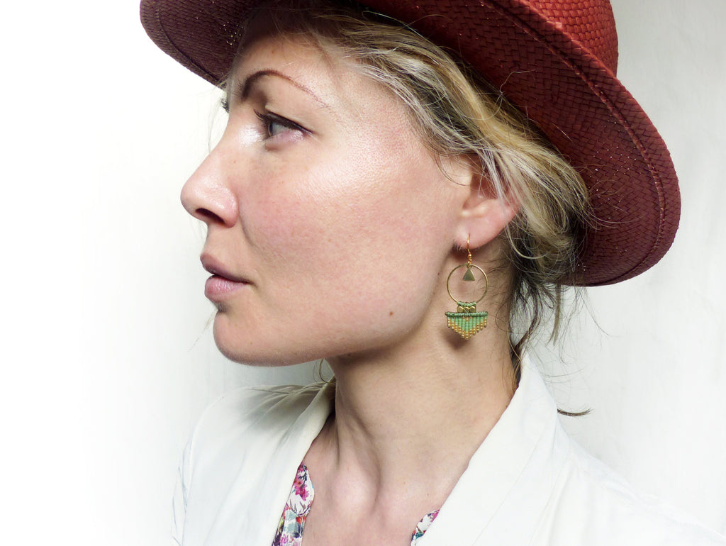 Peut inclure: Une femme portant un chapeau à larges bords avec une paire de boucles d'oreilles pendantes géométriques vertes et dorées. Les boucles d'oreilles présentent un petit cercle avec un triangle à l'intérieur et une frange de perles vertes et dorées.