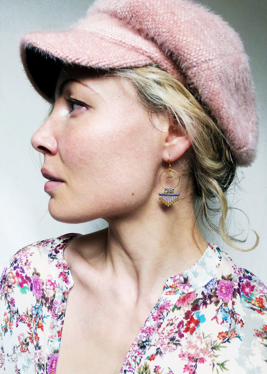 Peut inclure: Une femme portant une casquette de newsboy rose en fourrure et une blouse à fleurs avec des boucles d'oreilles en perles dorées et violettes.