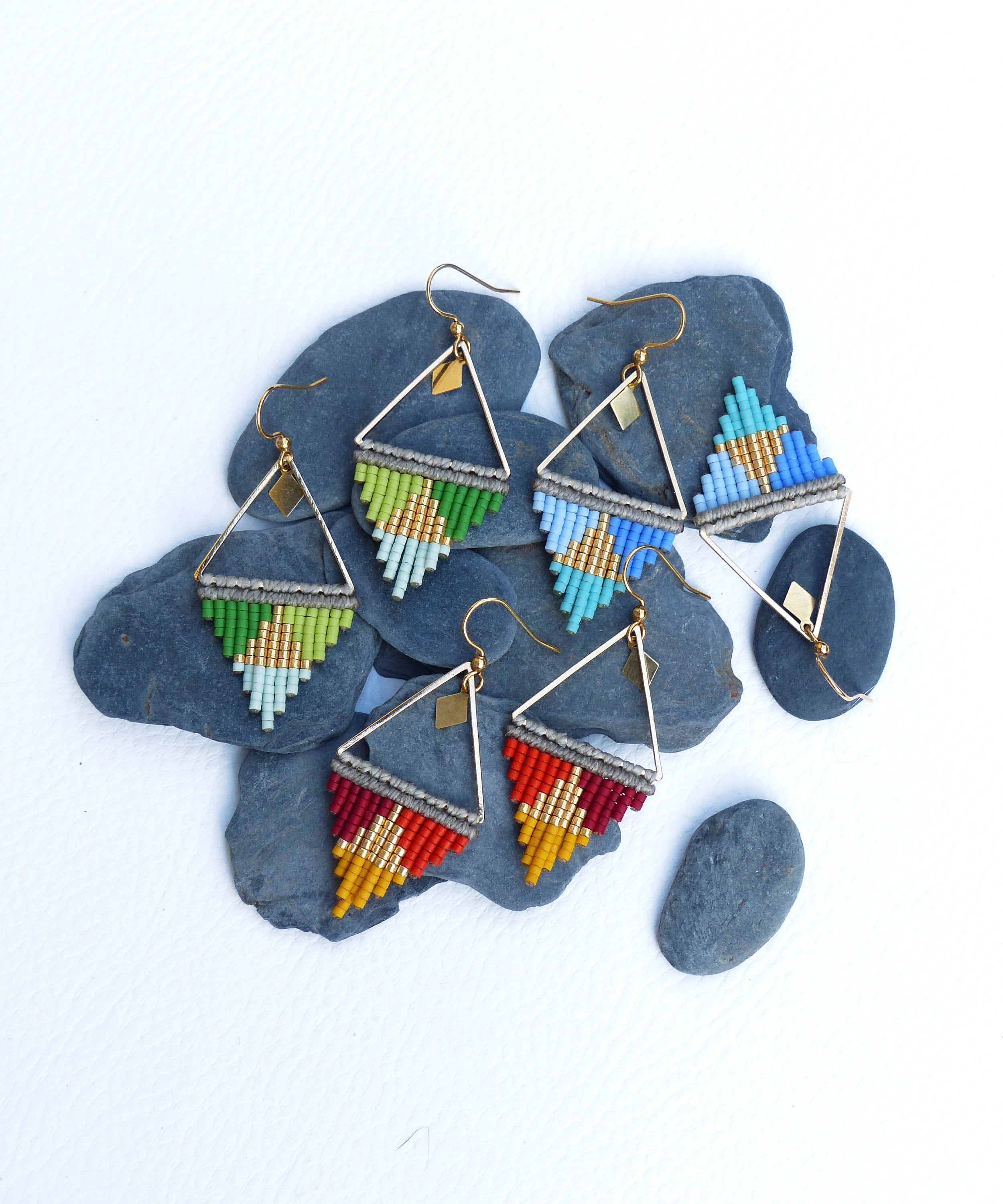 Peut inclure: Cinq paires de boucles d'oreilles de forme triangulaire avec des anneaux dorés et des franges de perles colorées. Les boucles d'oreilles sont présentées sur des pierres grises.