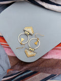 Peut inclure: Une paire de boucles d'oreilles créoles dorées avec une frange de perles blanches et dorées. Les boucles d'oreilles sont sur une surface grise.