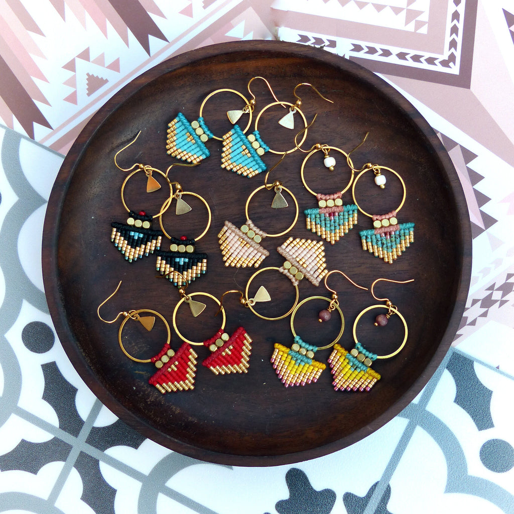 Peut inclure: Dix paires de boucles d'oreilles en perles avec des anneaux dorés et des détails en frange. Les boucles d'oreilles sont présentées sur un plateau en bois. La frange est de différentes couleurs, notamment turquoise, rose, rouge, jaune et noir.