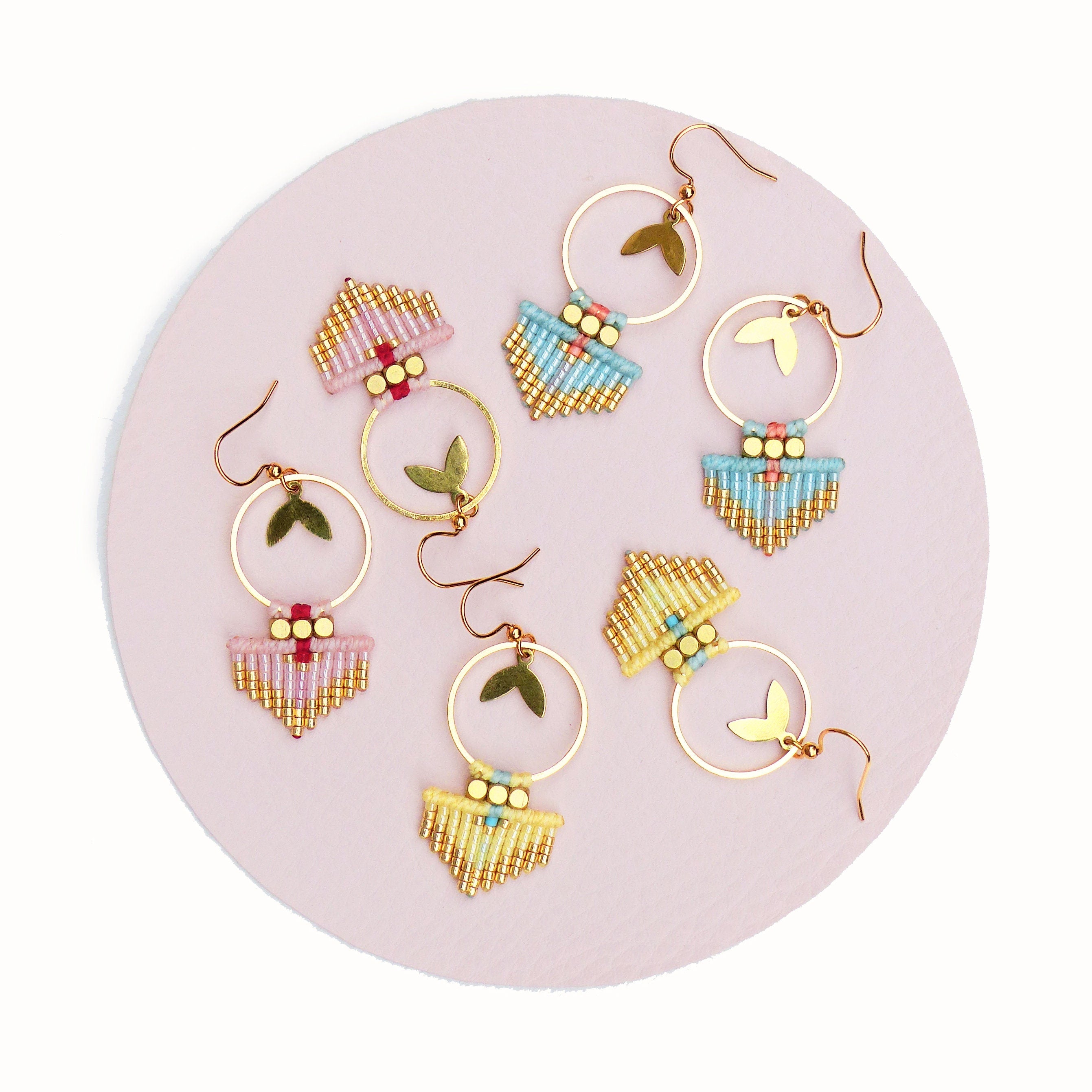 Peut inclure: Cinq paires de boucles d'oreilles en perles avec des cercles dorés et un pendentif doré. Les boucles d'oreilles sont dans des tons de rose, bleu et jaune.