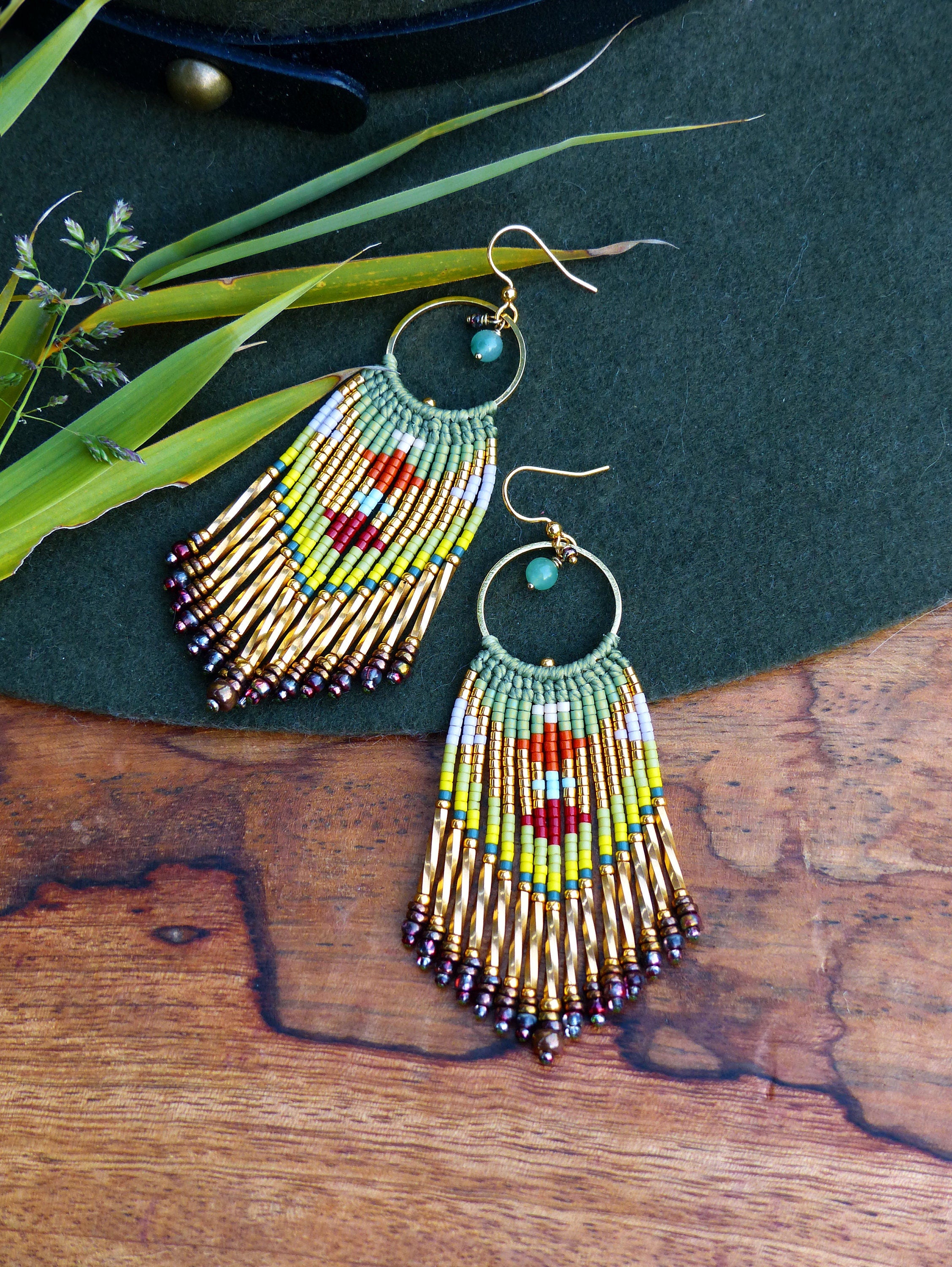 Peut inclure: Une paire de longues boucles d'oreilles en perles colorées avec des accents dorés. Les boucles d'oreilles présentent une perle de pierre verte au sommet de chaque boucle d'oreille et une frange de perles dorées au bas.