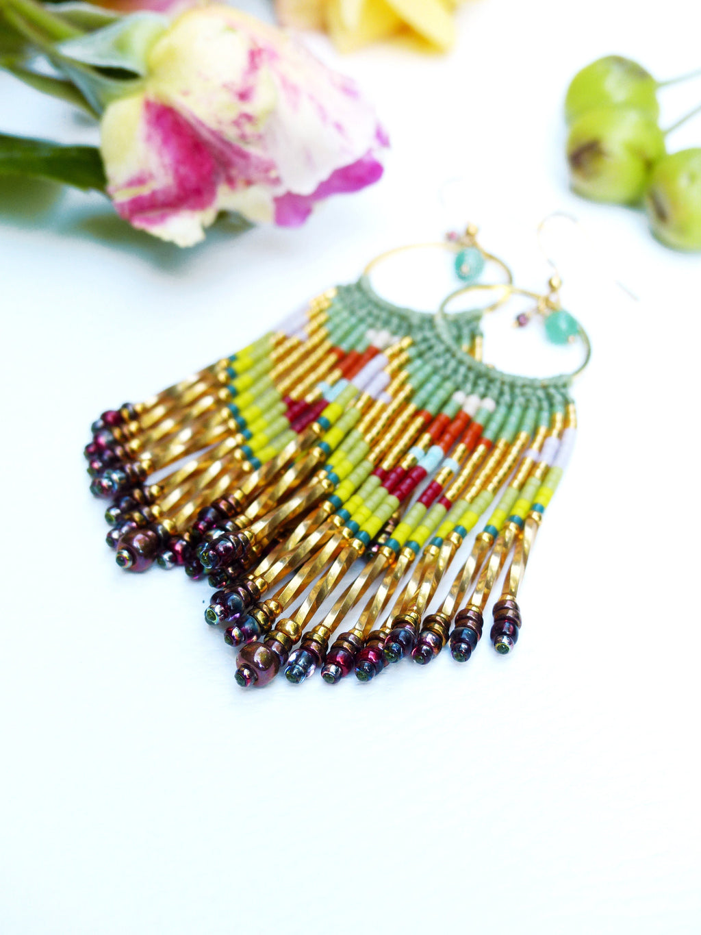 Peut inclure: Une paire de longues boucles d'oreilles en perles avec des cercles dorés et une frange de perles colorées. Les perles sont dans des tons de vert, jaune, rouge et violet.