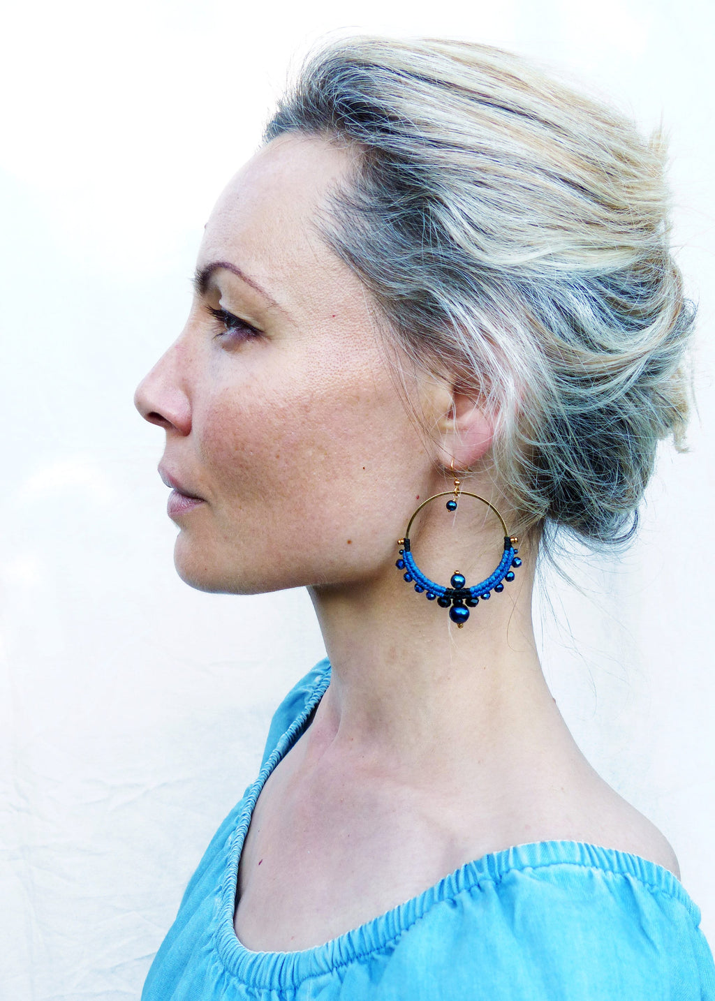 Peut inclure: Une femme aux cheveux blonds portant de grandes boucles d'oreilles avec des perles bleues et noires.