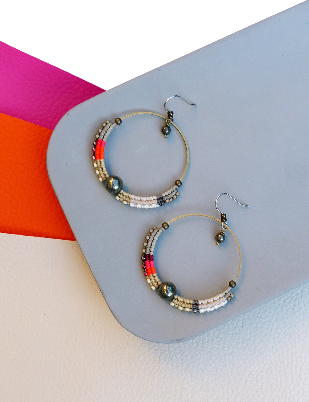 Peut inclure: Paire de boucles d'oreilles créoles avec une monture en métal doré. La moitié inférieure de chaque boucle est ornée d'un motif de petites perles blanches, grises, rouges et noires. Une grosse perle gris foncé est centrée sur chaque boucle.