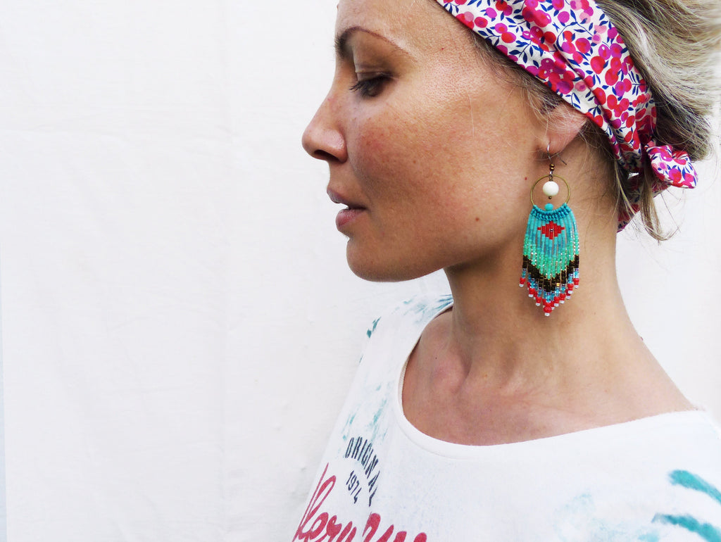 Peut inclure: Une femme portant une chemise blanche avec un bandeau floral et des boucles d'oreilles en perles turquoise, rouge et noires.