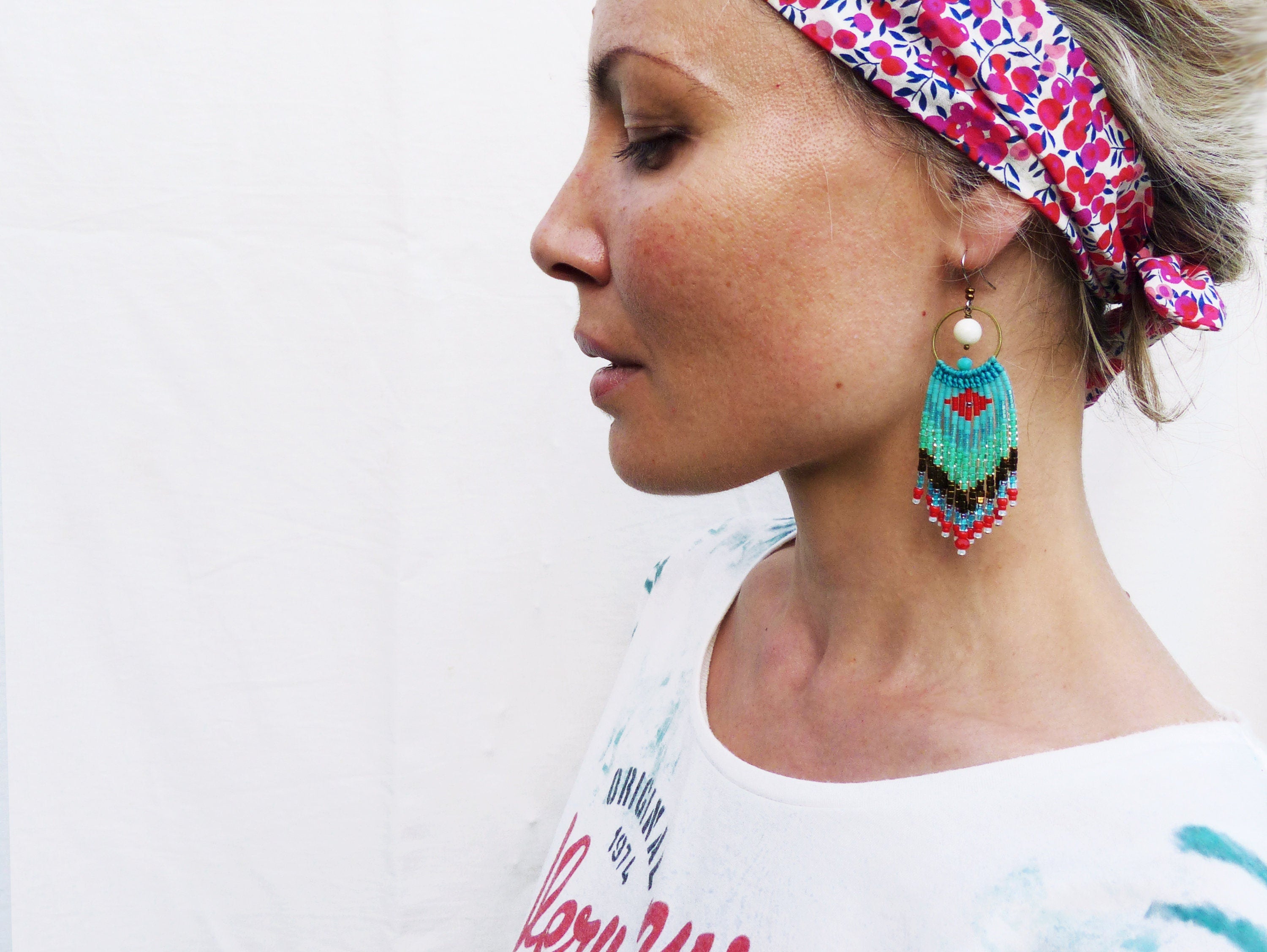 Peut inclure: Une femme portant une chemise blanche avec un bandeau floral et des boucles d'oreilles en perles turquoise, rouge et noires.