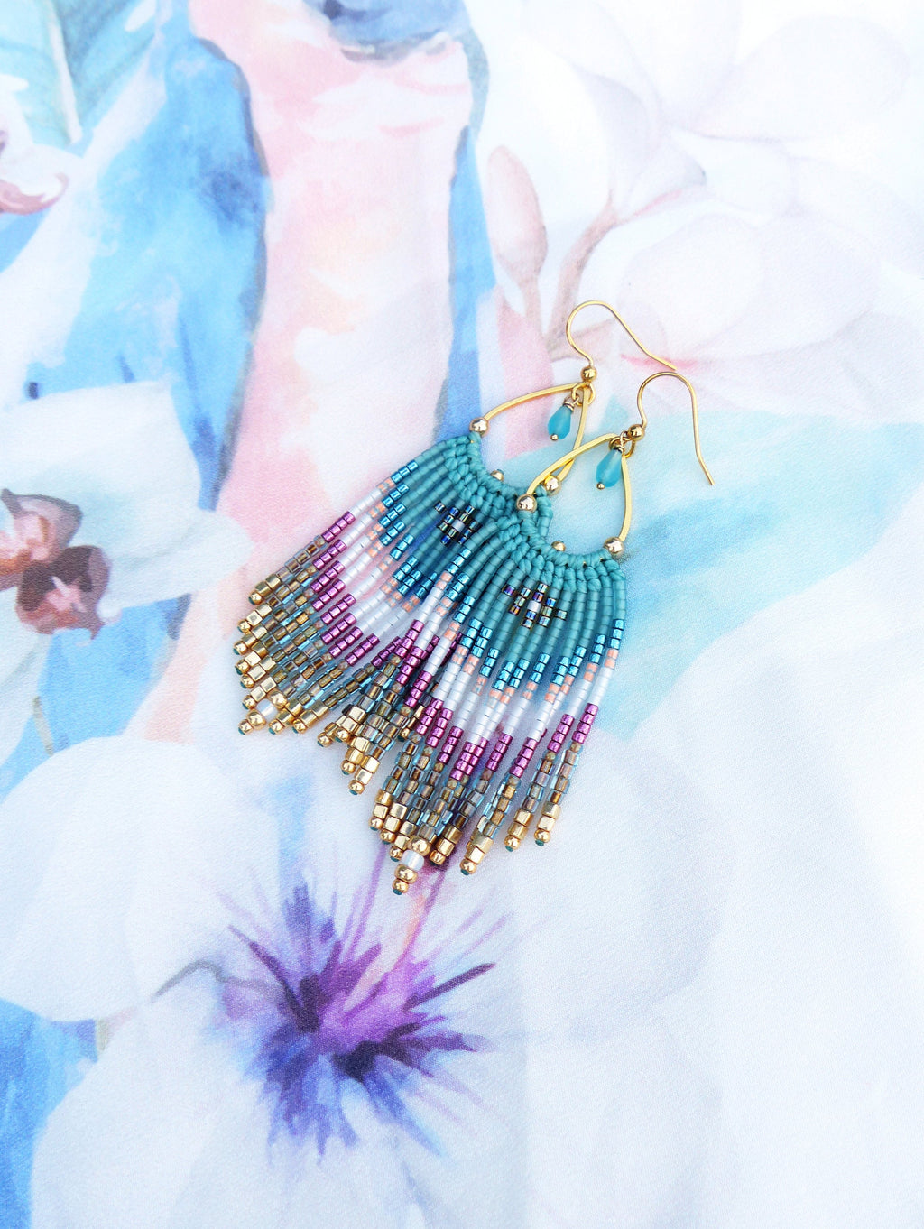 Peut inclure: Boucles d'oreilles pendantes dorées avec des perles turquoise, blanches et roses. Les boucles d'oreilles ont une forme de larme et sont faites avec une variété de perles.