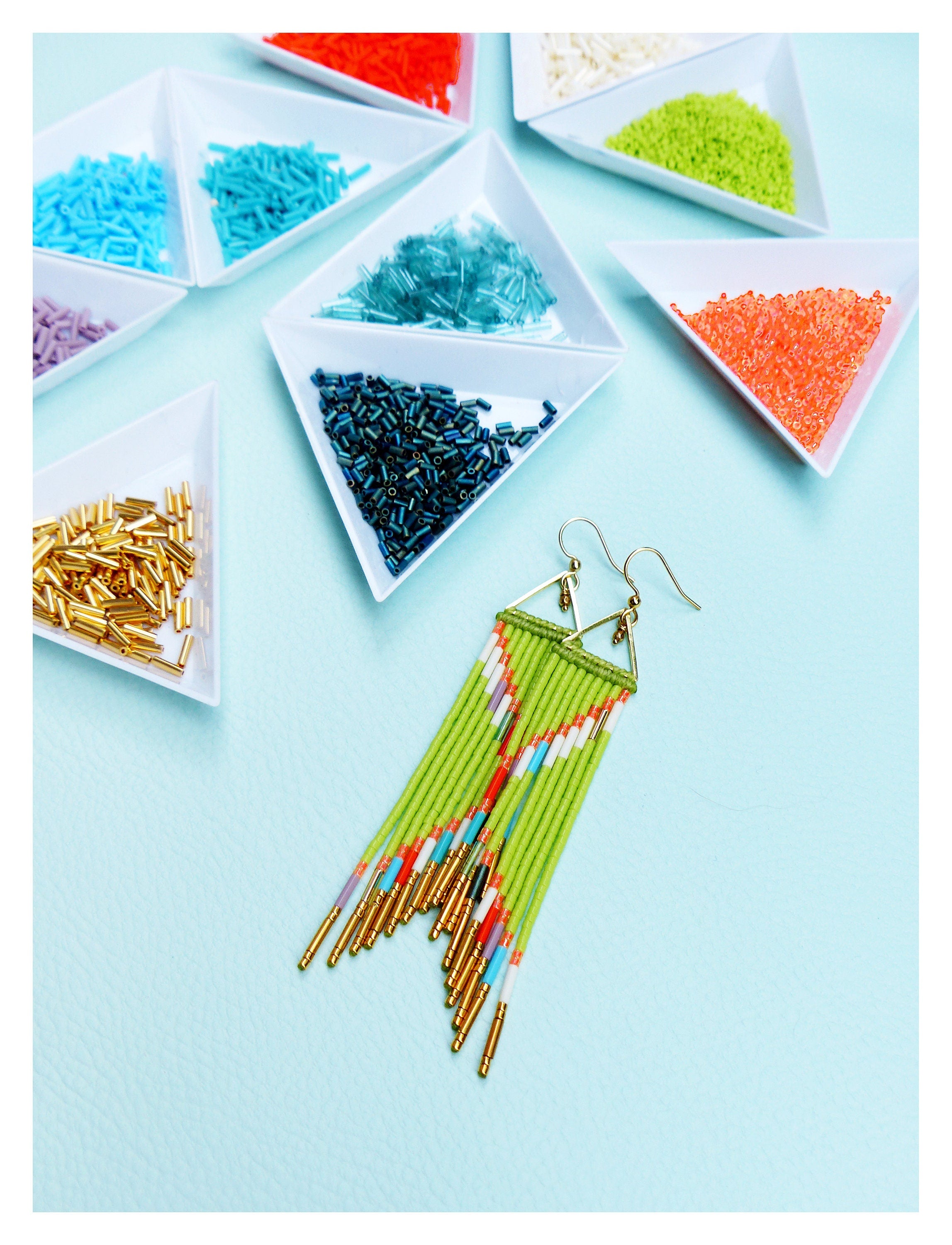 Peut inclure: Une paire de longues boucles d'oreilles en perles vertes avec des accents dorés. Les boucles d'oreilles sont faites avec une variété de perles colorées, y compris le blanc, le rouge et le bleu. Les boucles d'oreilles sont suspendues à des crochets dorés.