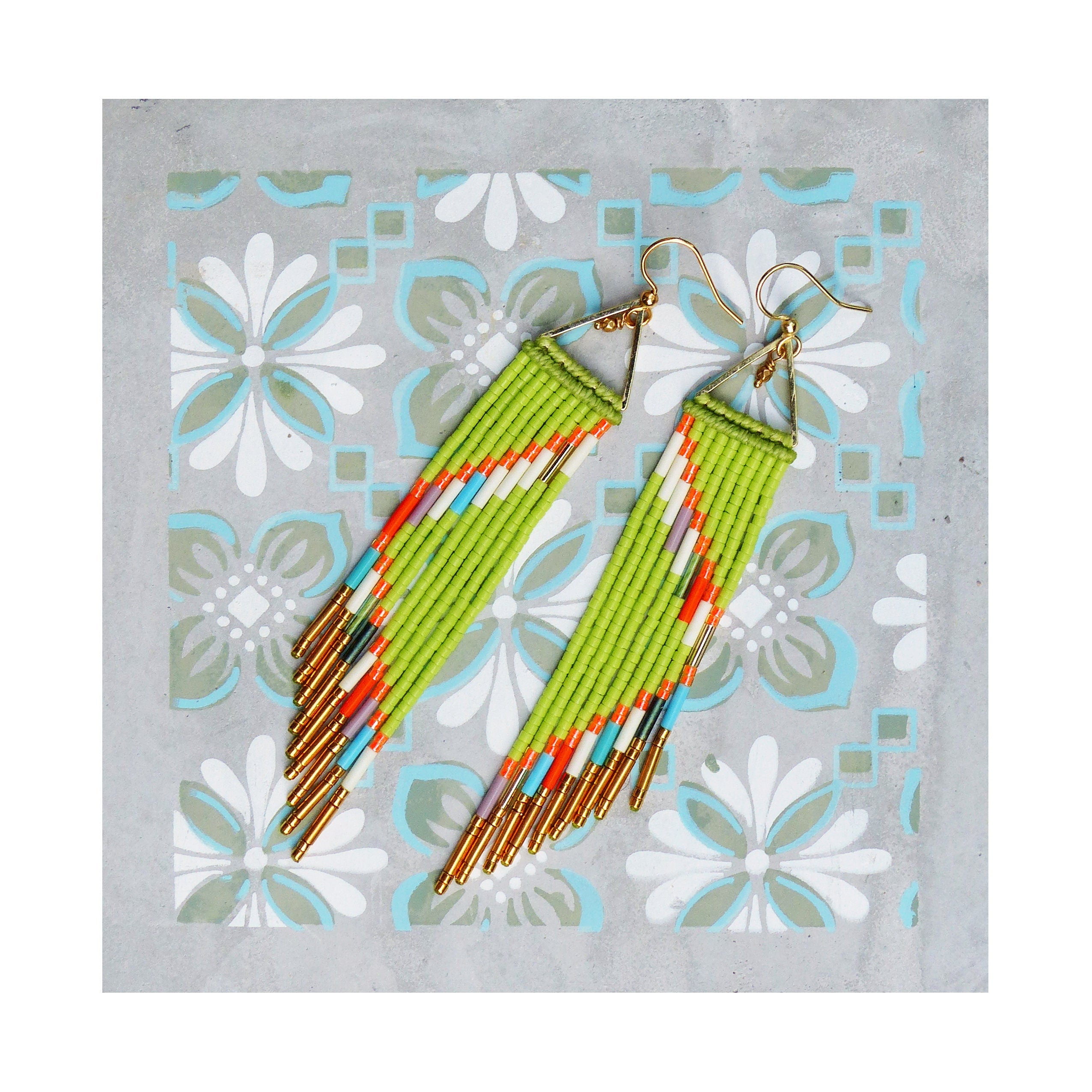 Peut inclure: Une paire de longues boucles d'oreilles en perles vertes avec des accents dorés. Les boucles d'oreilles sont faites avec une variété de perles colorées, y compris orange, blanc et bleu.