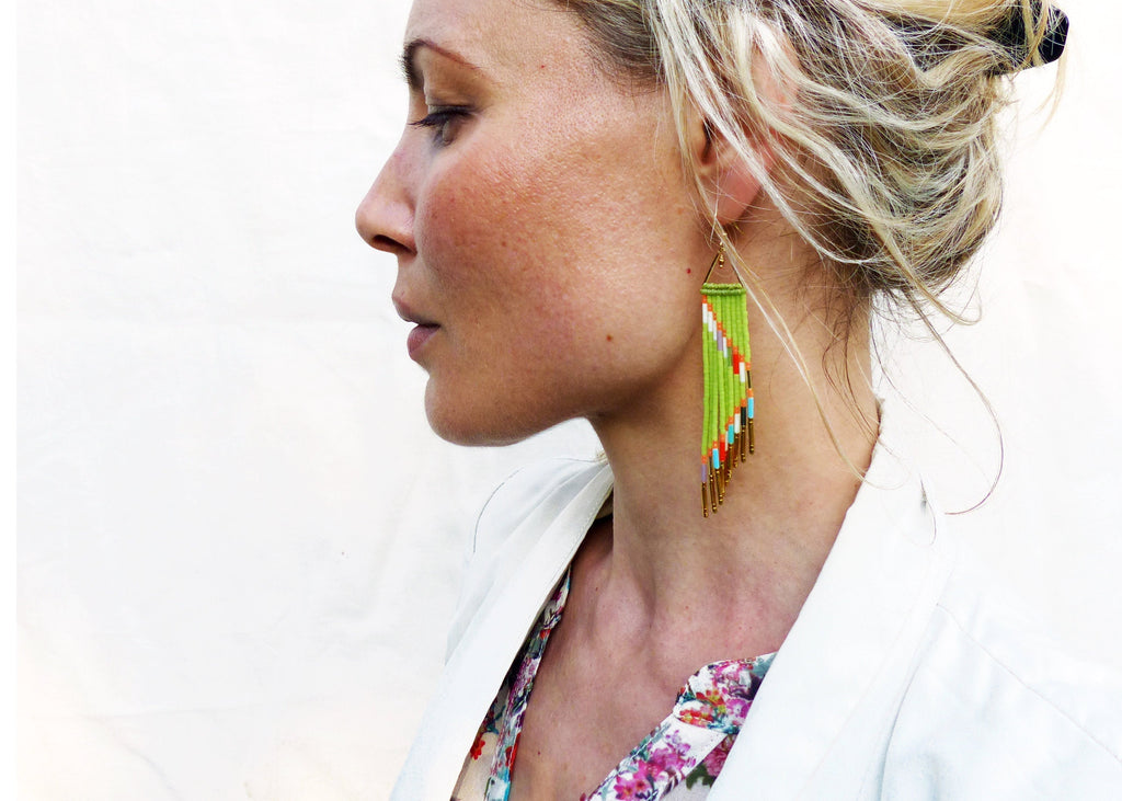 Peut inclure: Une femme portant un blazer blanc et une blouse à fleurs avec de longues boucles d'oreilles en perles vertes et dorées.