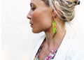 Peut inclure: Une femme portant un blazer blanc et une blouse à fleurs avec de longues boucles d'oreilles en perles vertes et dorées.