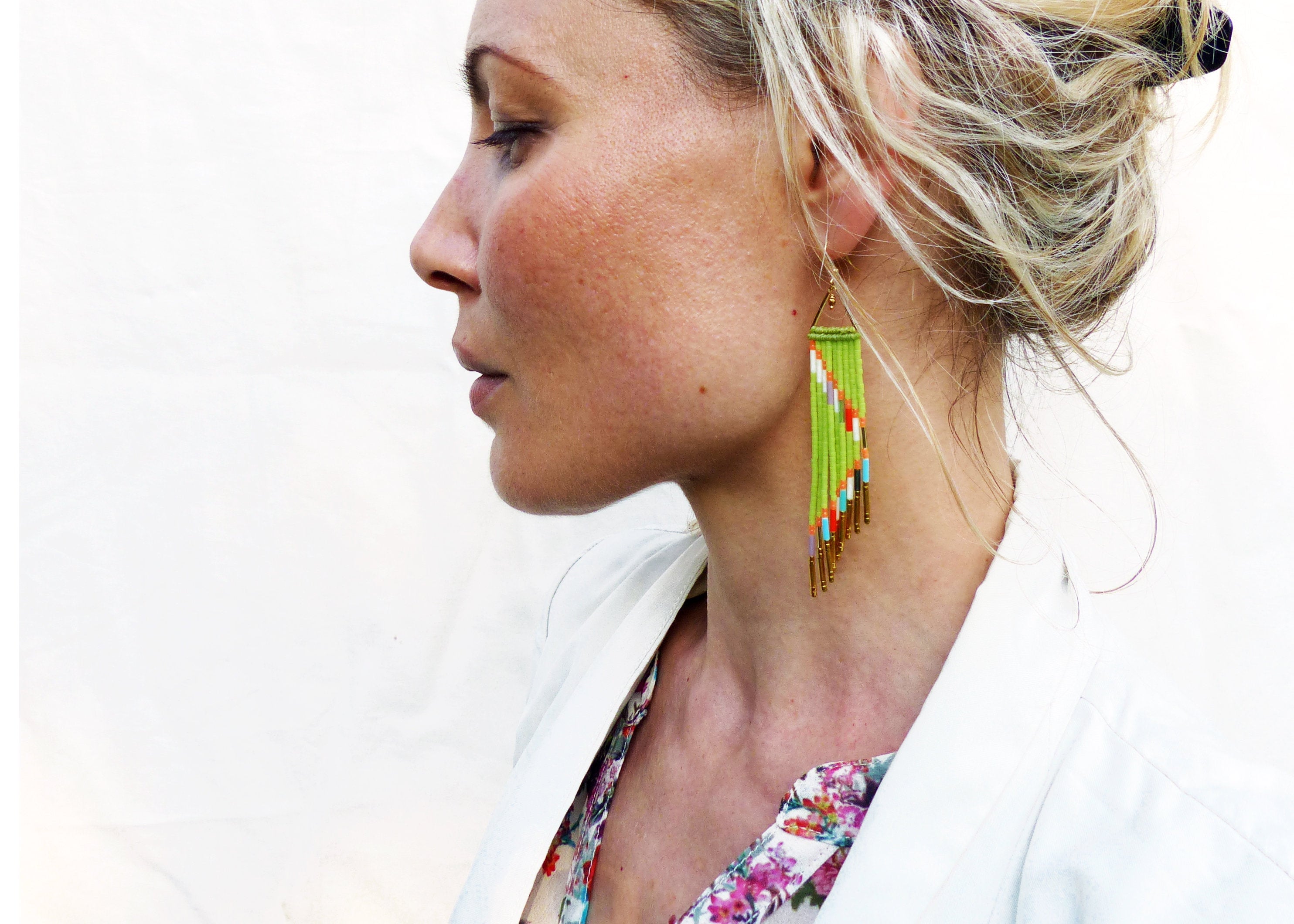 Peut inclure: Une femme portant un blazer blanc et une blouse à fleurs avec de longues boucles d'oreilles en perles vertes et dorées.