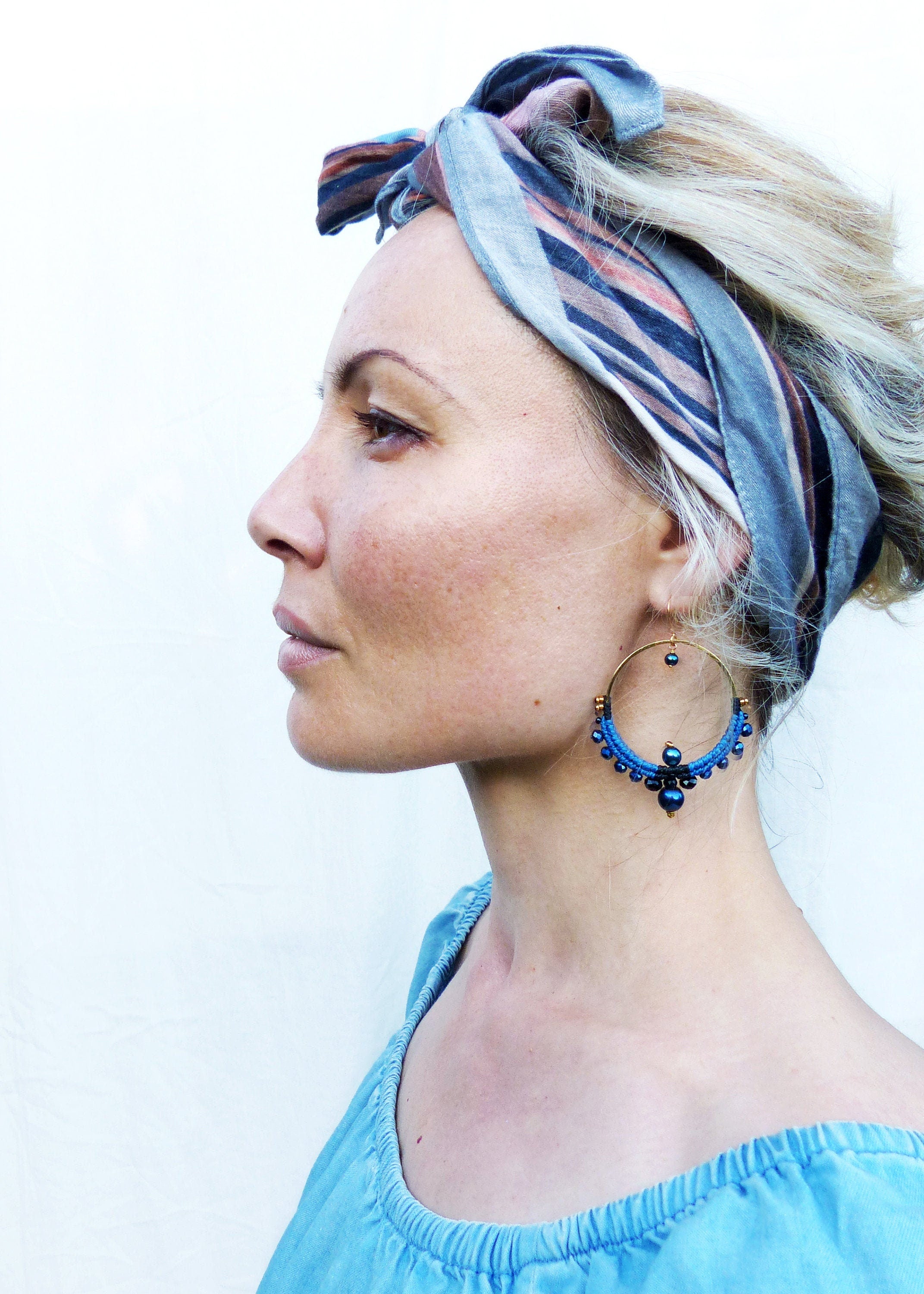Peut inclure: Une femme aux cheveux blonds porte un bandeau rayé bleu et marron et de grandes boucles d'oreilles créoles bleues avec des perles bleu foncé. Les boucles d'oreilles ont un anneau en métal doré.