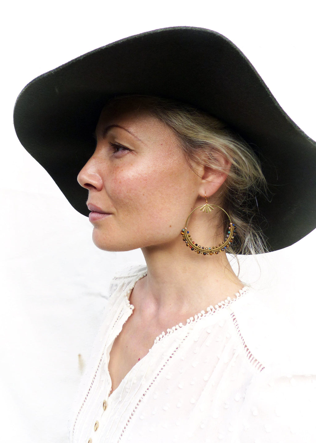 Peut inclure: Une femme portant un chapeau noir à larges bords et une blouse en dentelle blanche avec des boucles d'oreilles créoles dorées ornées de perles colorées.