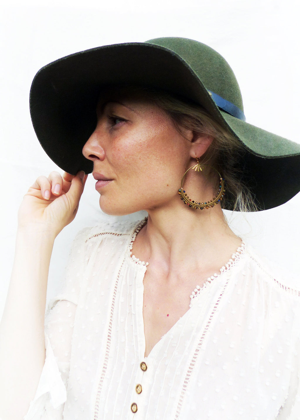 Peut inclure: Une femme portant un chapeau à larges bords vert et une blouse en dentelle blanche avec des boucles d'oreilles créoles dorées ornées de perles colorées.