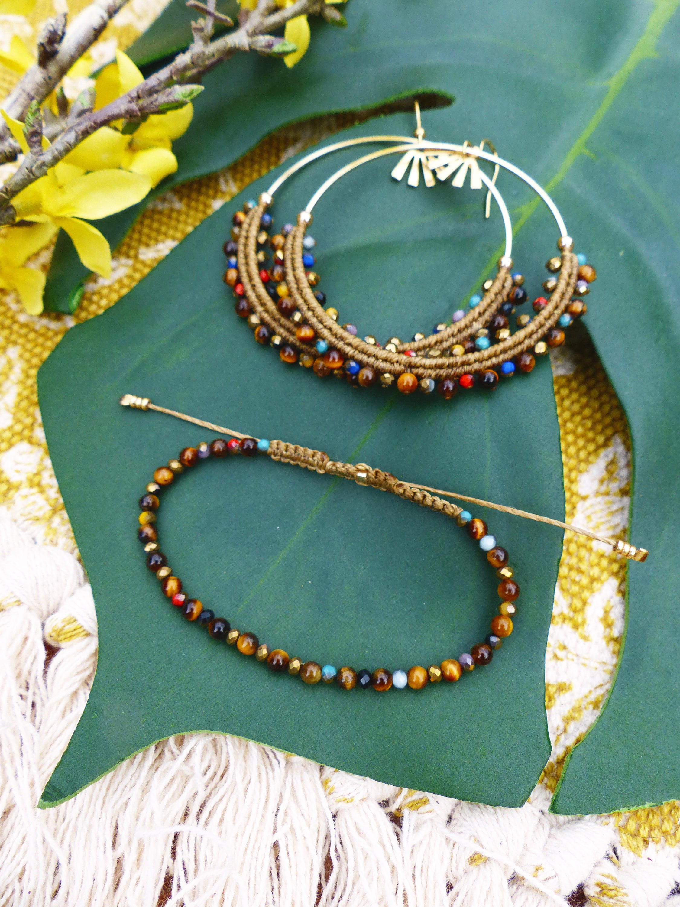 Peut inclure: Une paire de boucles d'oreilles créoles dorées avec des perles brunes et multicolores, et un bracelet en perles brunes avec des perles œil de tigre.
