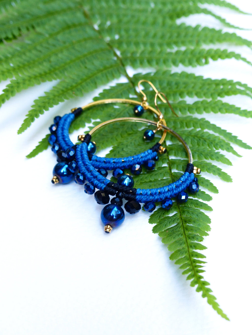 Peut inclure: Une paire de boucles d'oreilles créoles bleues et noires avec des accents dorés. Les boucles d'oreilles sont faites de fil tissé et présentent des perles bleues et noires.