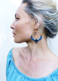 Peut inclure: Une femme portant un haut bleu décolleté avec de grandes boucles d'oreilles en forme de cerceau ornées de perles bleues et noires.