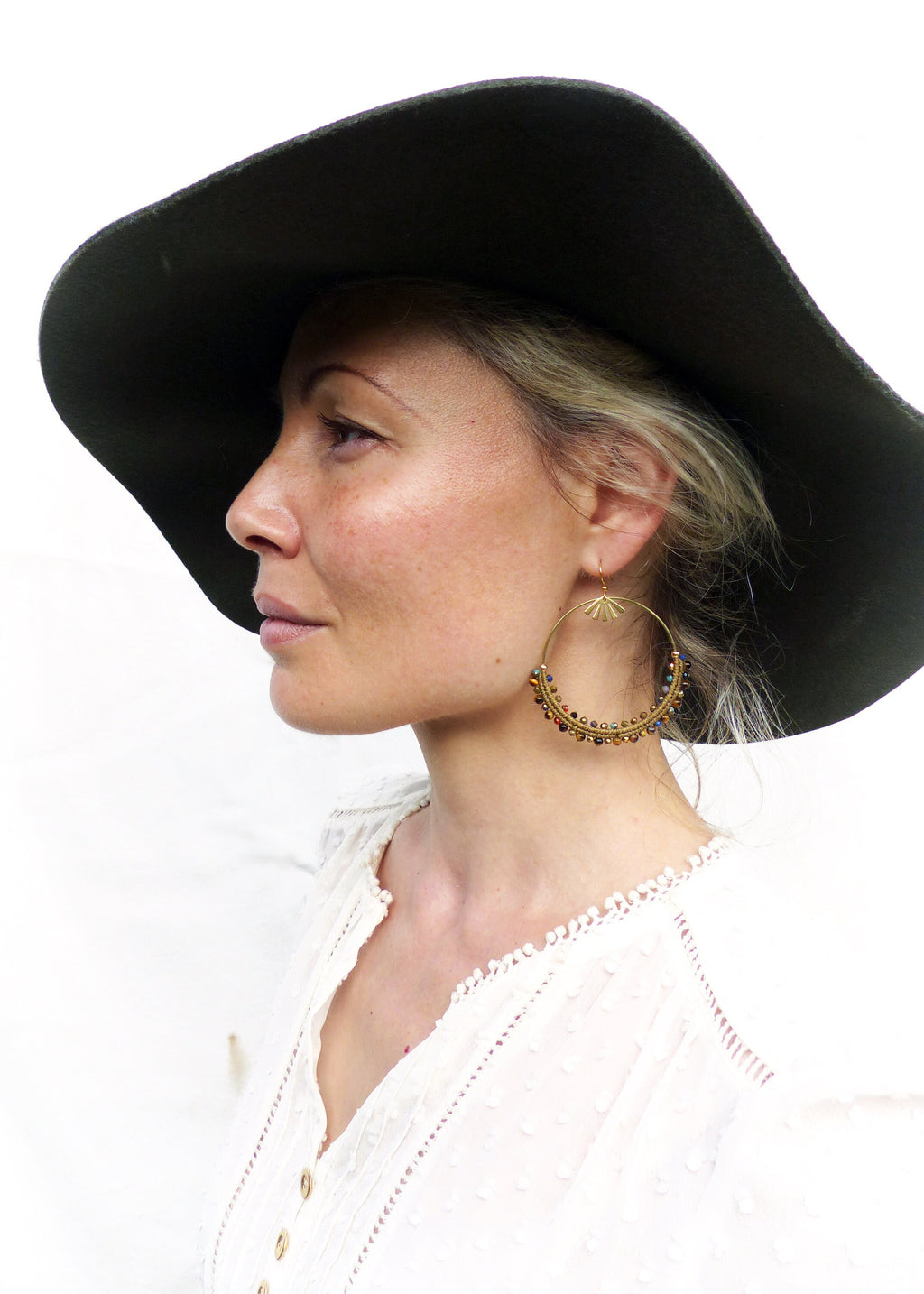 Peut inclure: Une femme portant un chapeau noir à larges bords et une blouse en dentelle blanche avec des boucles d'oreilles créoles dorées ornées de perles colorées.