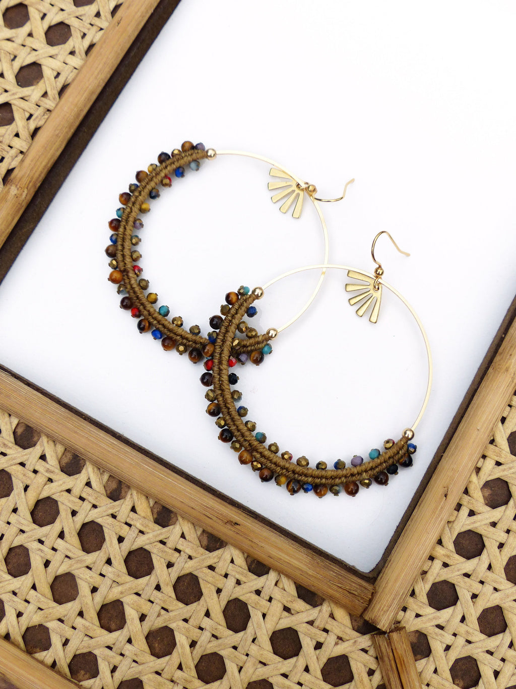 Peut inclure: Une paire de boucles d'oreilles créoles dorées avec des perles brunes et multicolores. Les boucles d'oreilles ont un motif en forme d'éventail en haut.