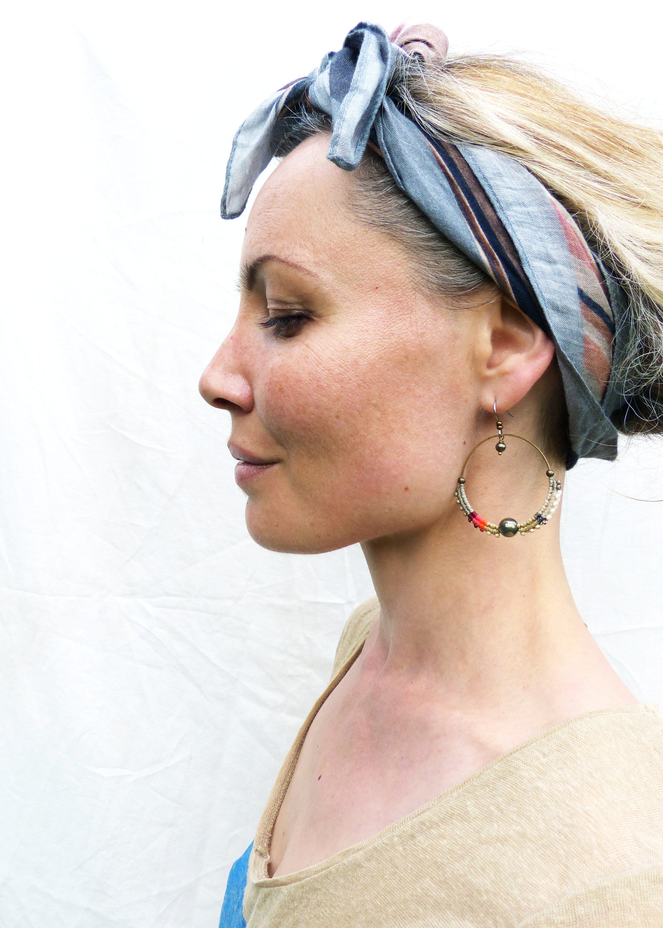 Peut inclure: Une personne portant des boucles d'oreilles créoles dorées avec des perles colorées et un foulard à motifs. Les boucles d'oreilles ont une grosse perle foncée au centre et sont ornées de perles rouges, vertes et blanches. Le foulard est bleu, marron et rose.