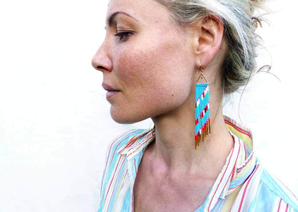 Peut inclure: Une paire de longues boucles d'oreilles en turquoise avec des accents dorés. Les boucles d'oreilles présentent un motif géométrique avec des perles rouges, blanches et noires.