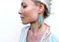 Peut inclure: Une paire de longues boucles d'oreilles en turquoise avec des accents dorés. Les boucles d'oreilles présentent un motif géométrique avec des perles rouges, blanches et noires.