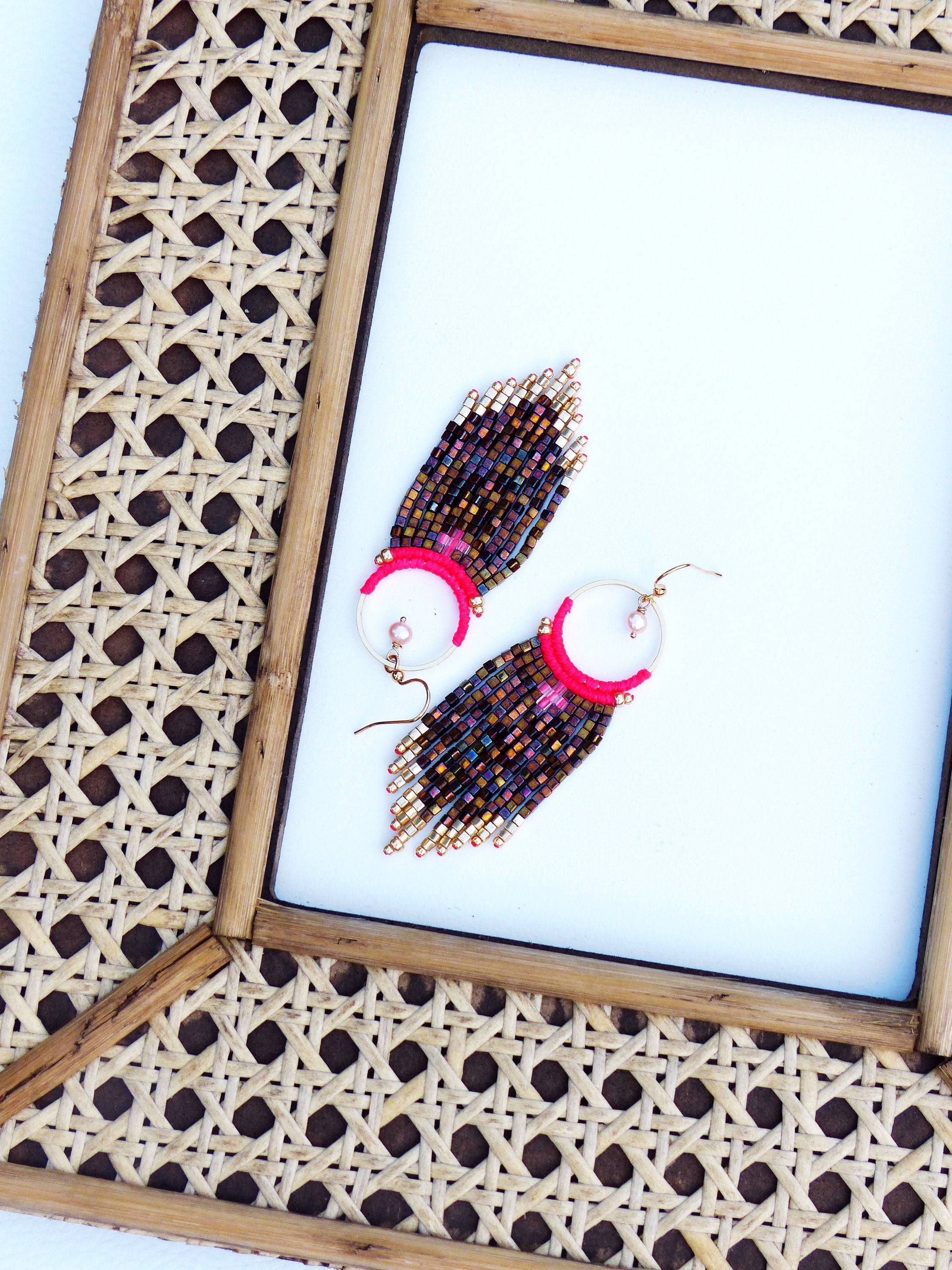 Peut inclure: Une paire de boucles d'oreilles en perles avec un motif rose et or. Les boucles d'oreilles sont suspendues à un cadre tissé.