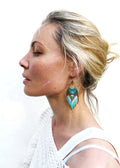 Peut inclure: Profil d'une personne portant une boucle d'oreille en perles turquoise, blanches et dorées. La boucle d'oreille a une forme de ventilateur avec un dessus en métal doré. La personne porte un haut blanc.