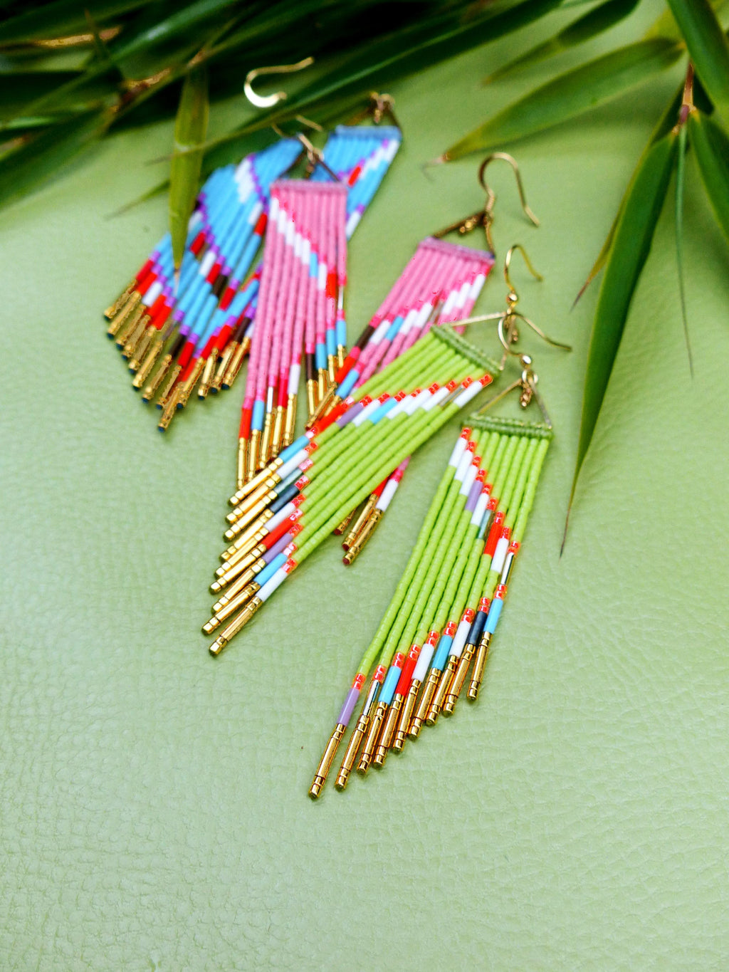 Peut inclure: Une paire de longues boucles d'oreilles en perles avec un motif géométrique. Les boucles d'oreilles sont faites de perles vertes, roses, bleues et blanches et ont des accents dorés.