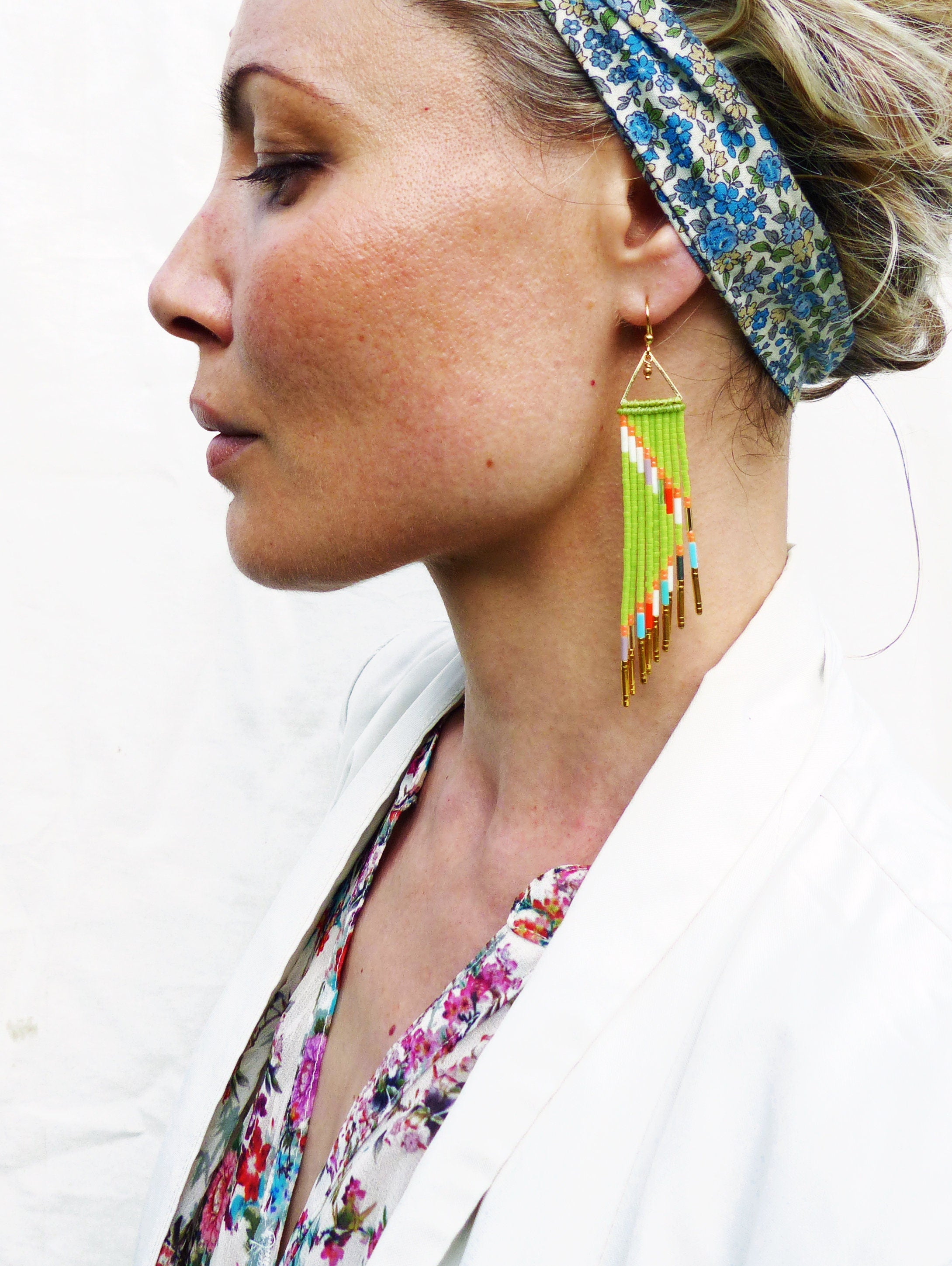 Peut inclure: Une paire de boucles d'oreilles en forme de glands vertes et dorées avec des accents colorés. Les boucles d'oreilles sont longues et pendent des lobes des oreilles.