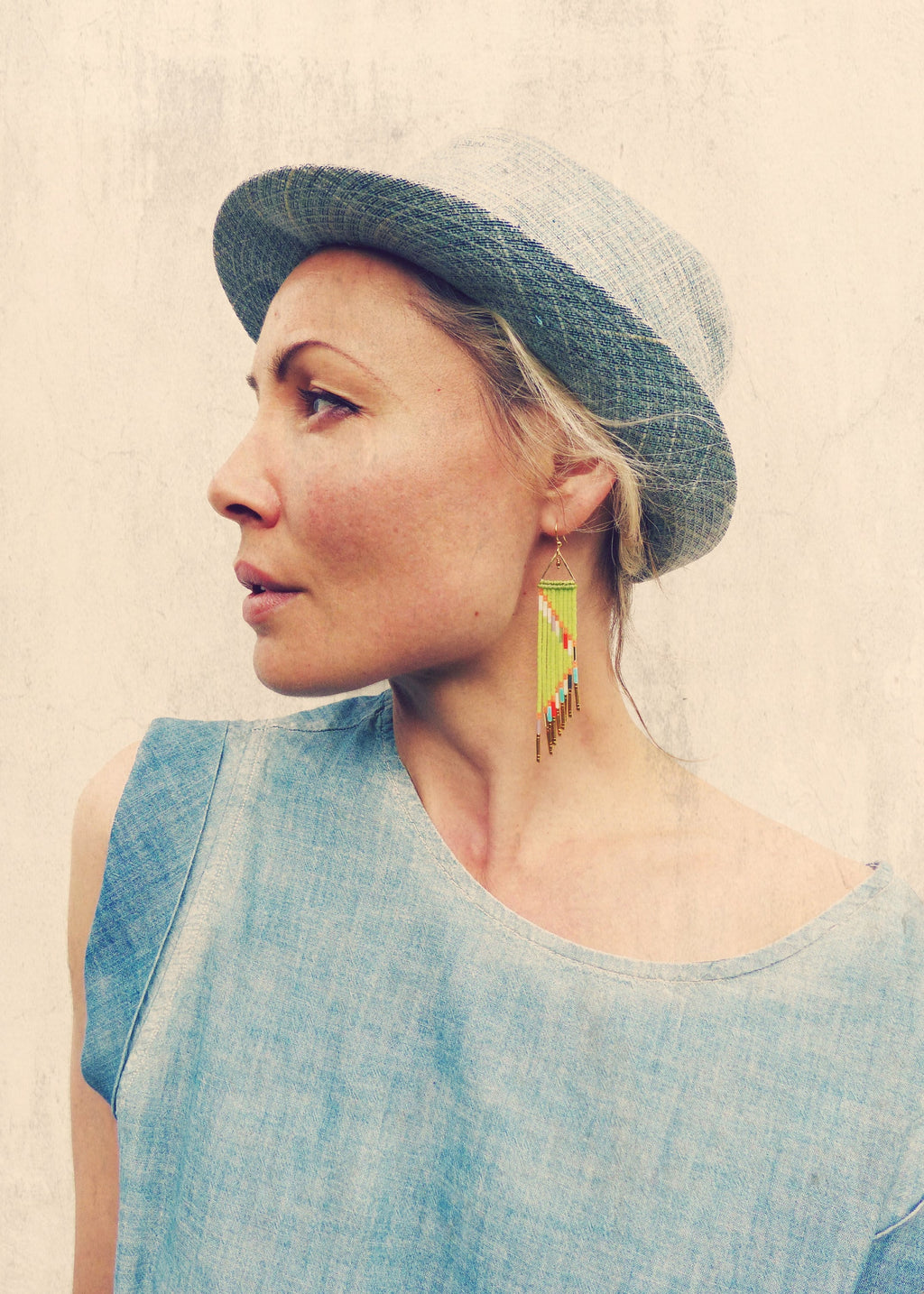 Peut inclure: Une femme portant une robe en jean bleu et un chapeau gris et blanc avec une boucle d'oreille en perles vertes et dorées.