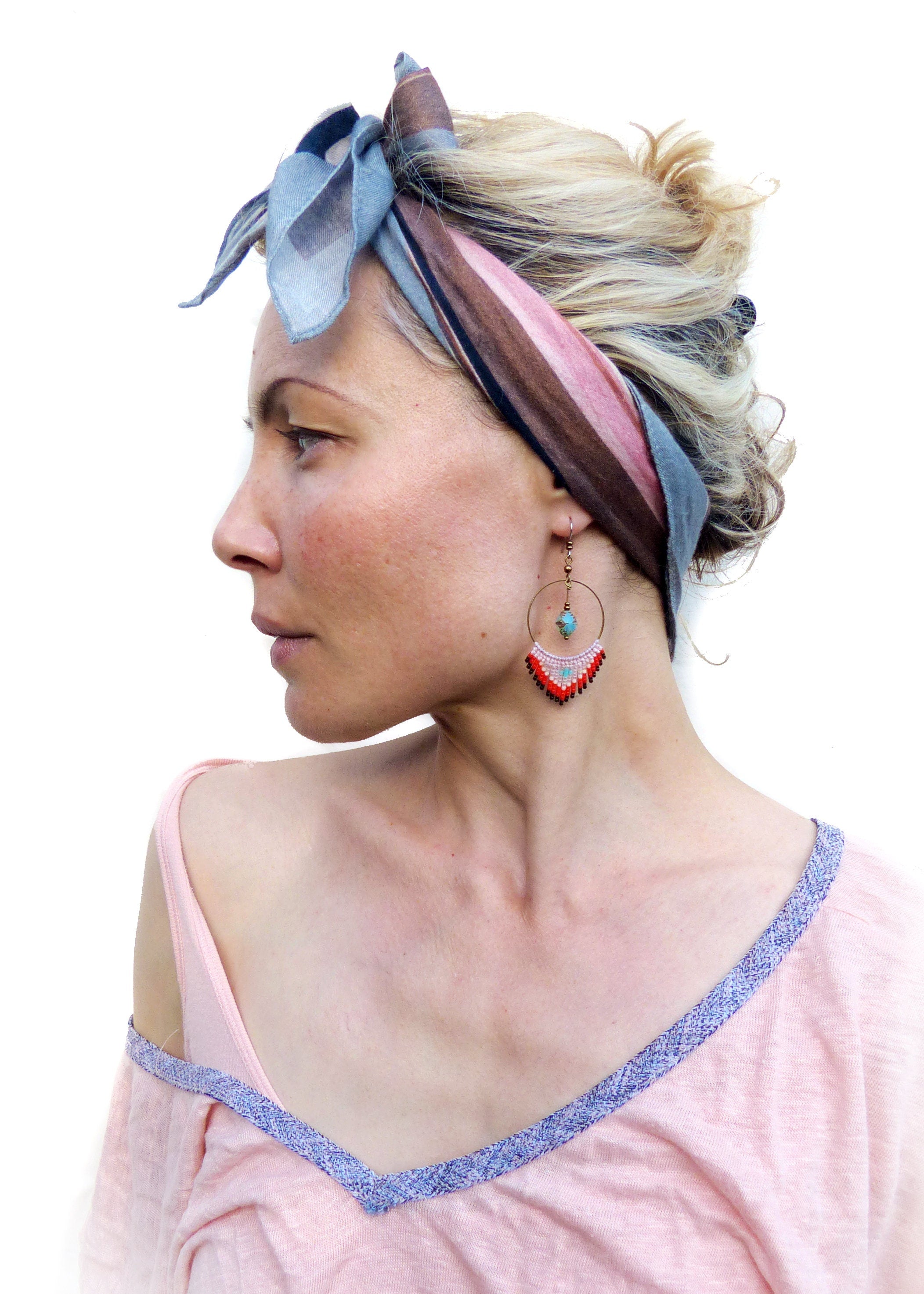 Peut inclure: Une femme aux cheveux blonds portant un bandana rose et marron et un t-shirt rose avec des bordures bleues. Elle porte des boucles d'oreilles créoles avec des perles rouges, blanches et turquoise.