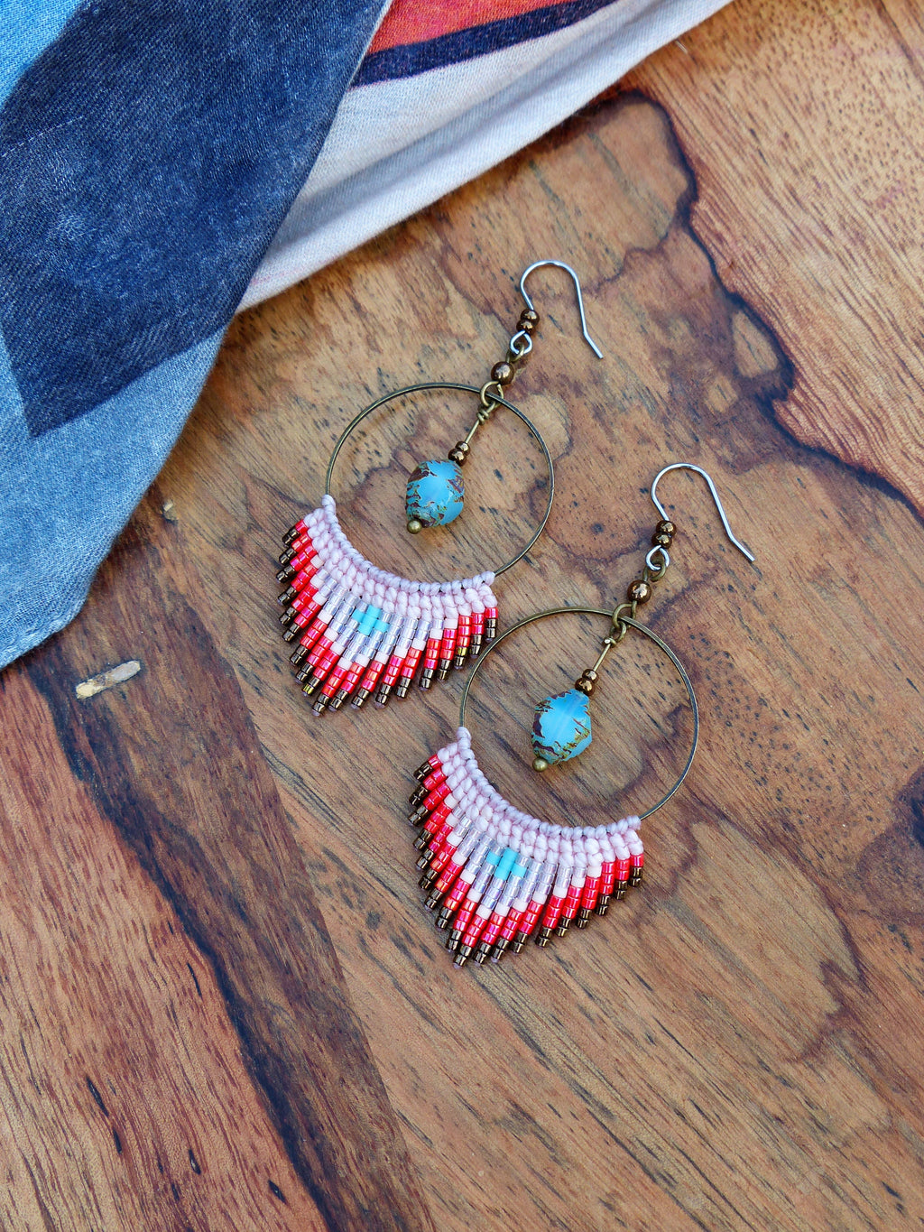 Peut inclure: Une paire de boucles d'oreilles créoles avec une frange de perles roses, rouges et brunes. Les créoles sont en métal et ont une perle turquoise qui pend.