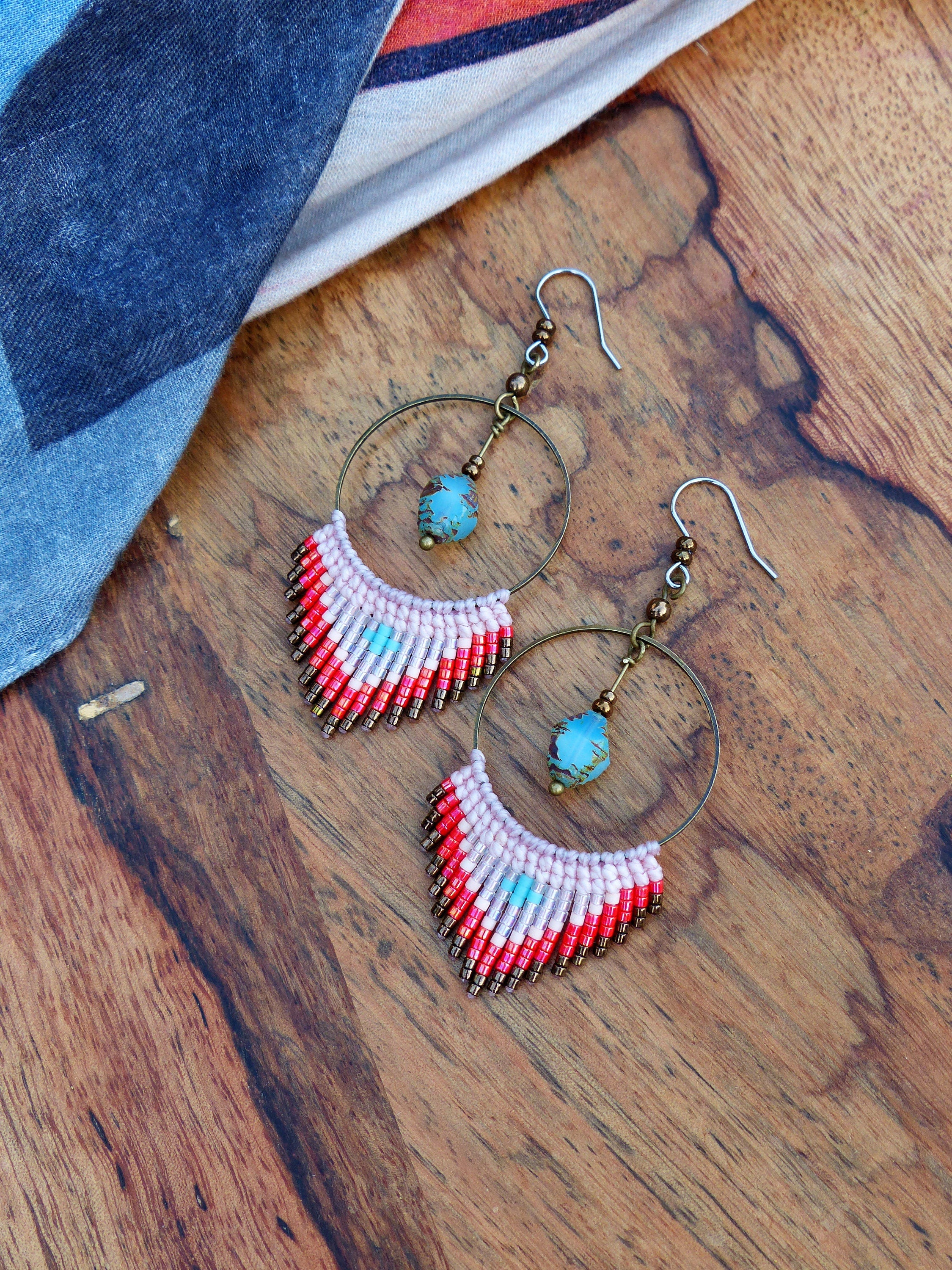 Peut inclure: Une paire de boucles d'oreilles créoles avec une frange de perles roses, rouges et brunes. Les créoles sont en métal et ont une perle turquoise qui pend.