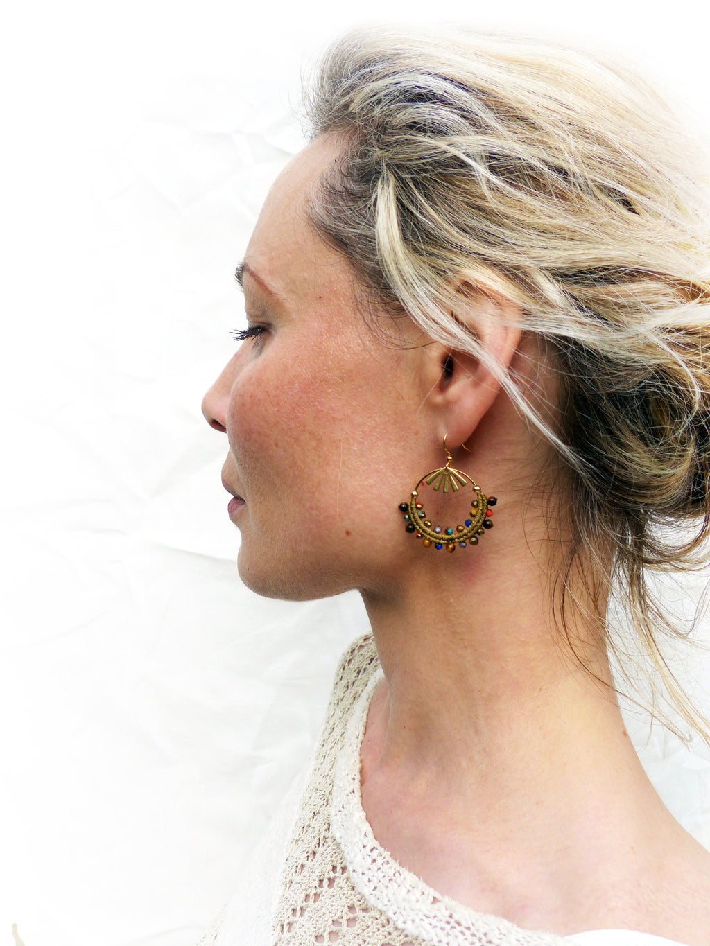 Peut inclure: Une femme portant un haut en crochet blanc avec des boucles d'oreilles créoles dorées ornées de perles colorées.