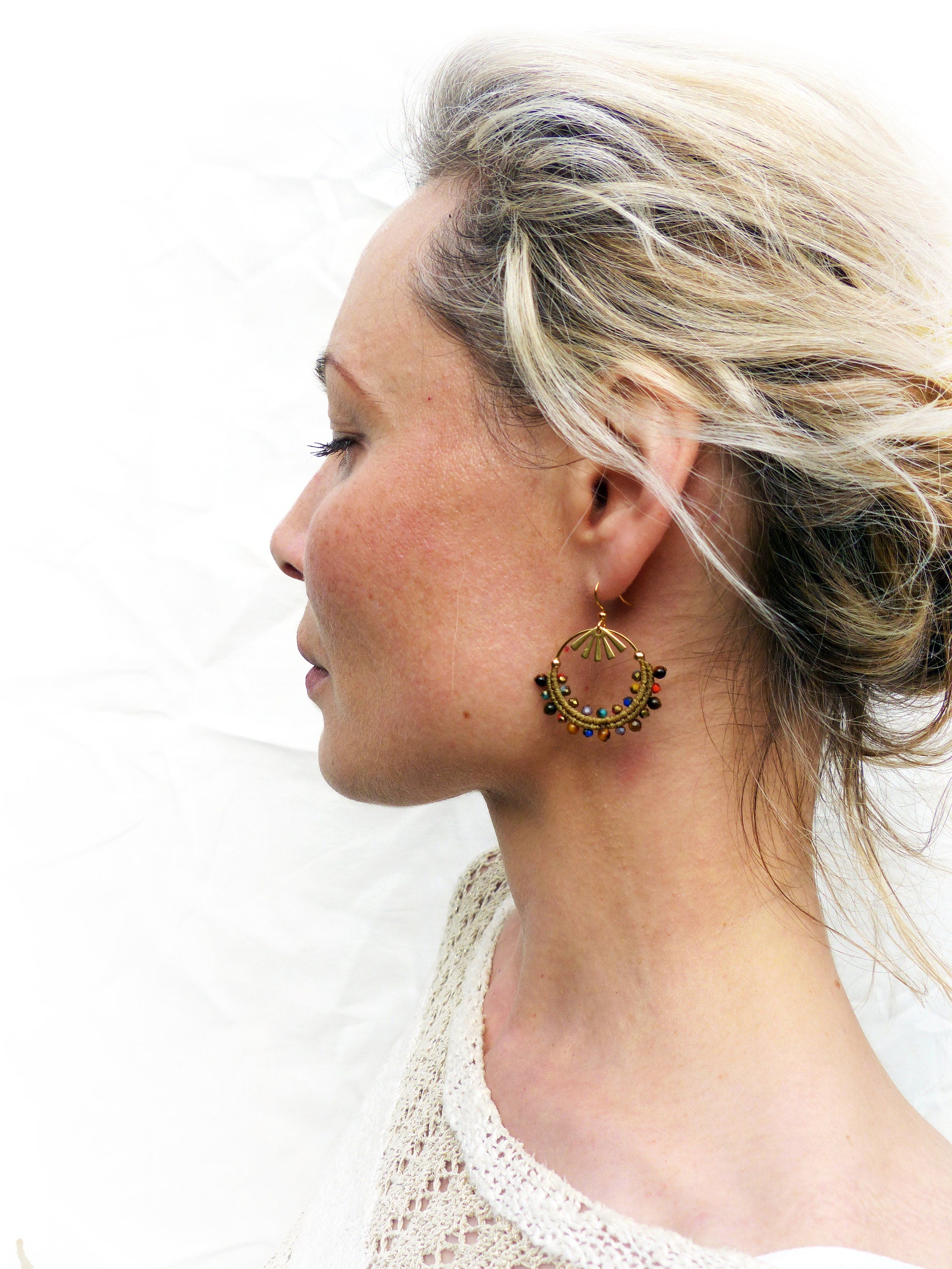 Peut inclure: Une femme portant un haut en crochet blanc avec des boucles d'oreilles créoles dorées ornées de perles colorées.