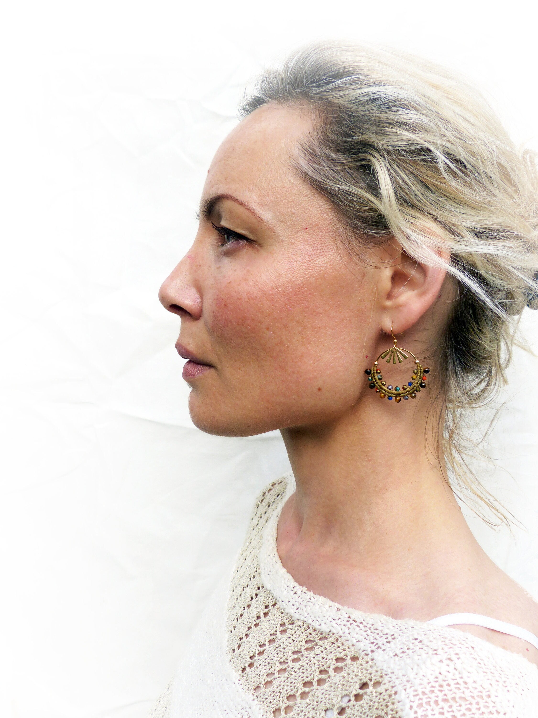 Peut inclure: Une femme aux cheveux blonds portant des boucles d'oreilles en or avec des perles colorées. Les boucles d'oreilles ont la forme d'un croissant de lune.