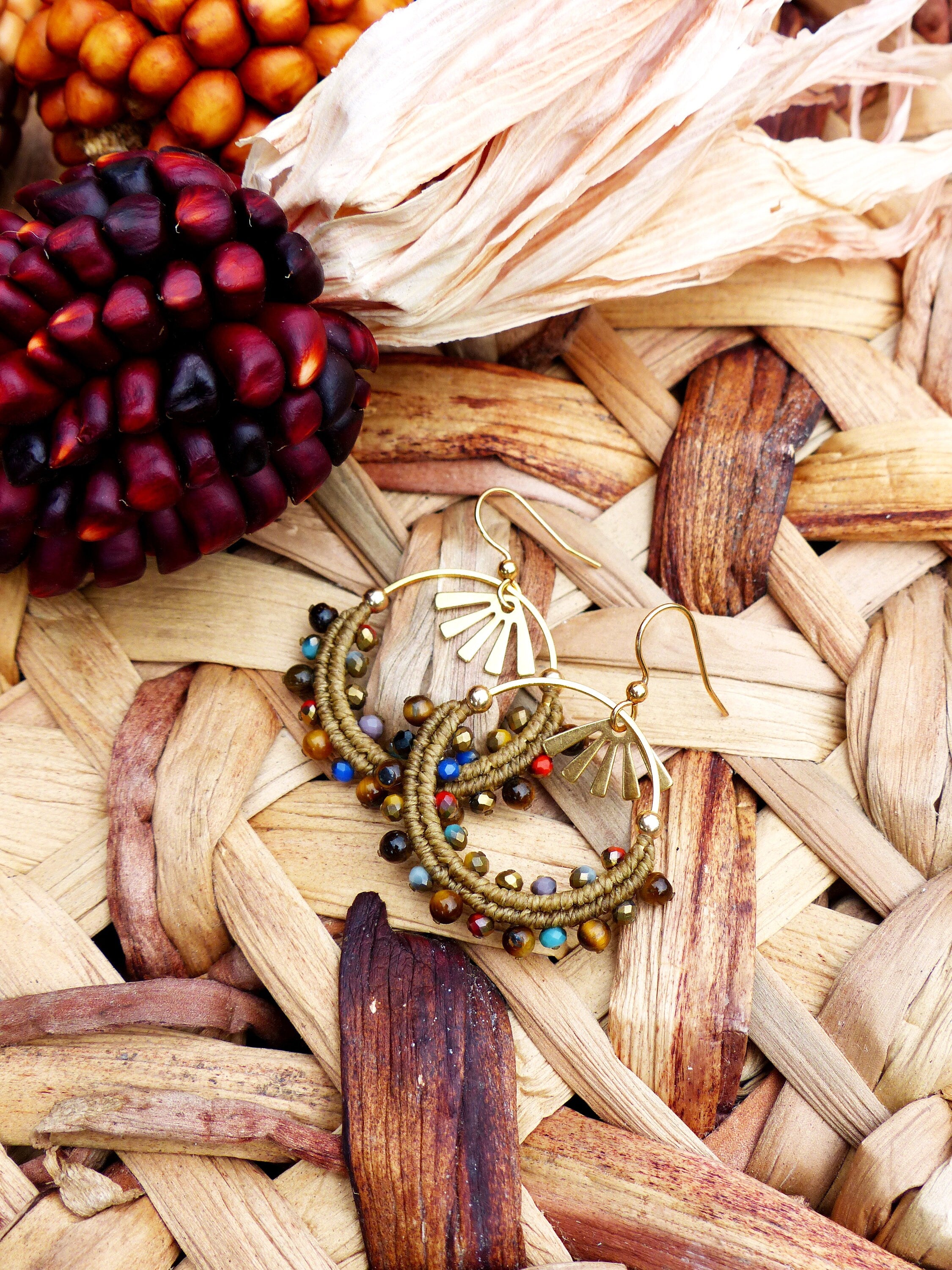 Peut inclure: Une paire de boucles d'oreilles créoles dorées avec des perles brunes et multicolores. Les boucles d'oreilles sont sur une surface en osier tressé.