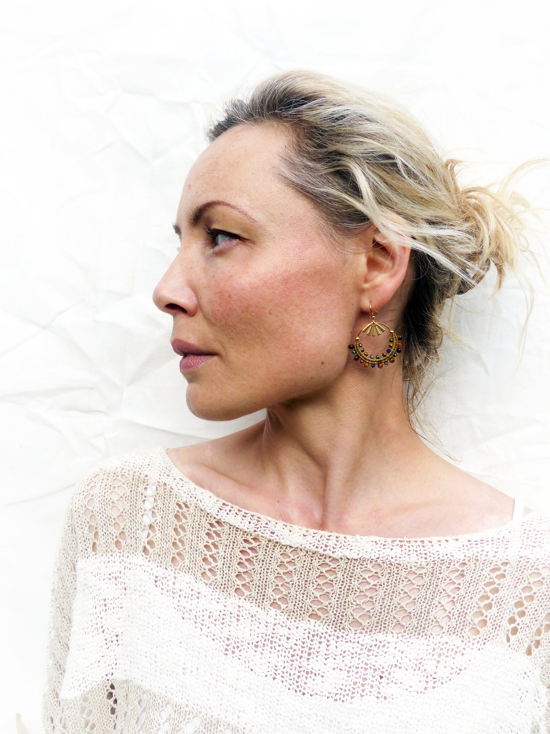 Peut inclure: Une femme aux cheveux blonds portant un haut en crochet blanc et des boucles d'oreilles créoles dorées avec des perles brunes.