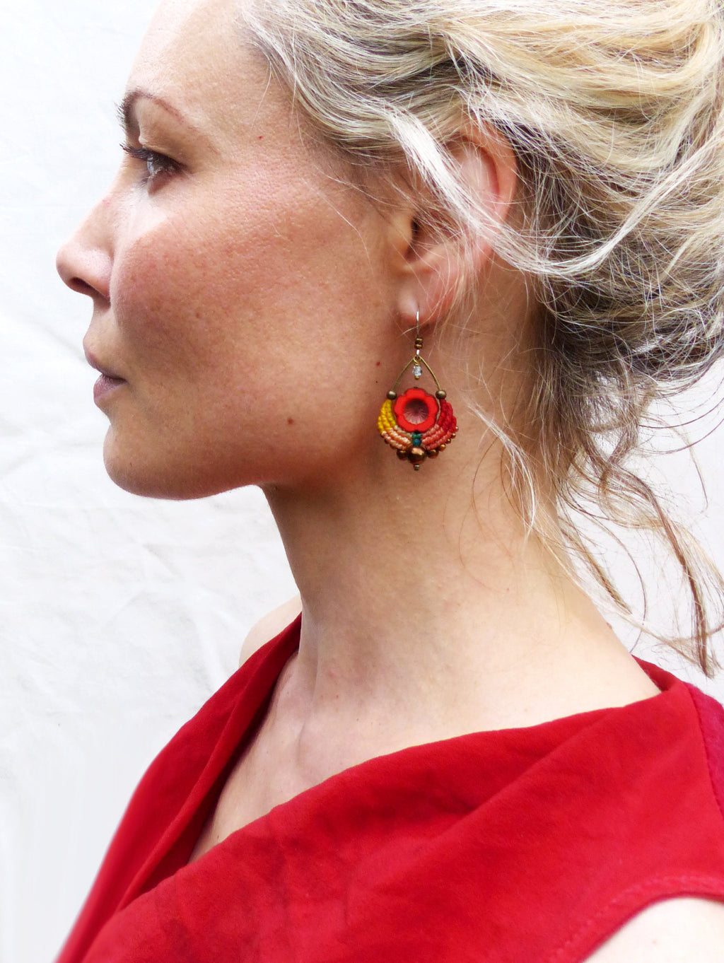 Peut inclure: Une femme portant une robe rouge avec une paire de boucles d'oreilles pendantes. Les boucles d'oreilles sont faites de perles rouges, orange et jaunes avec une petite pierre ronde et transparente au centre.